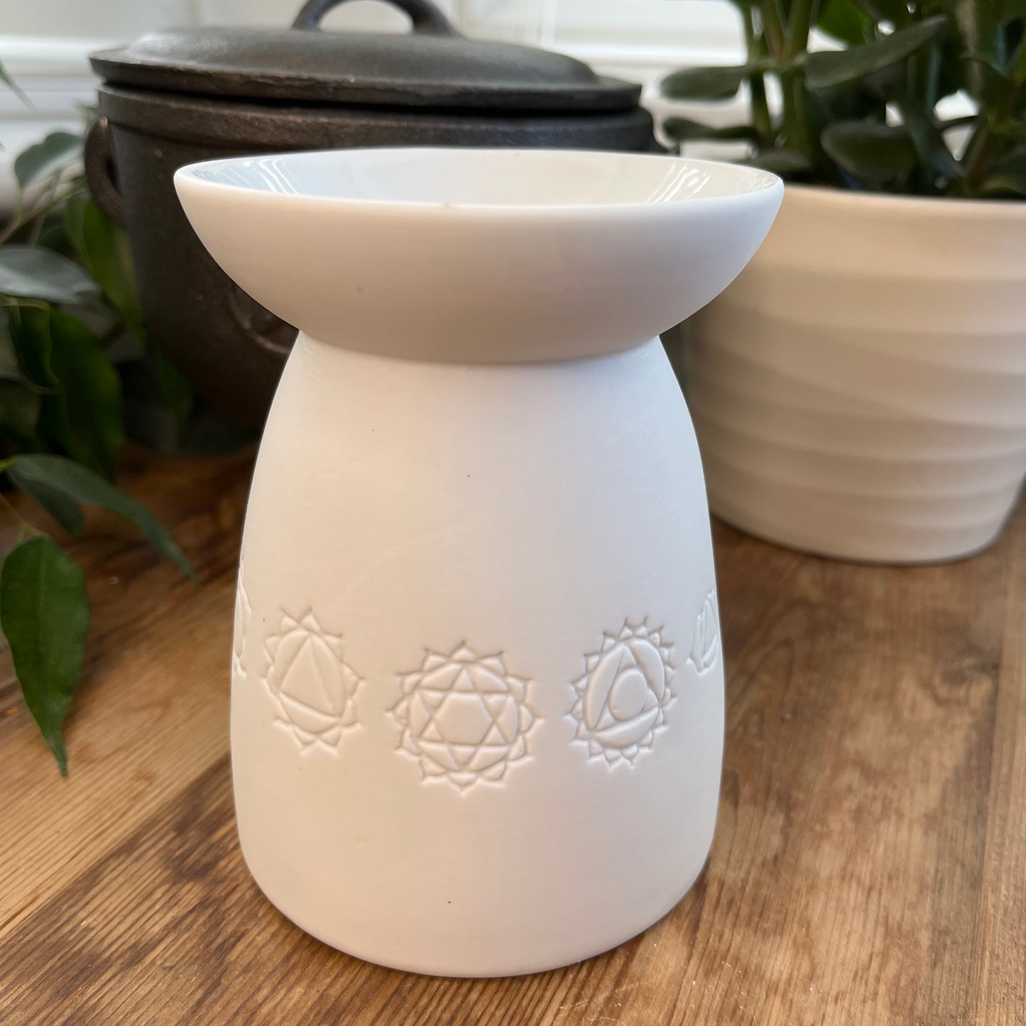 White ceramic oil burner with the symbols of the seven chakras itched around it. Pictured next to wax melts