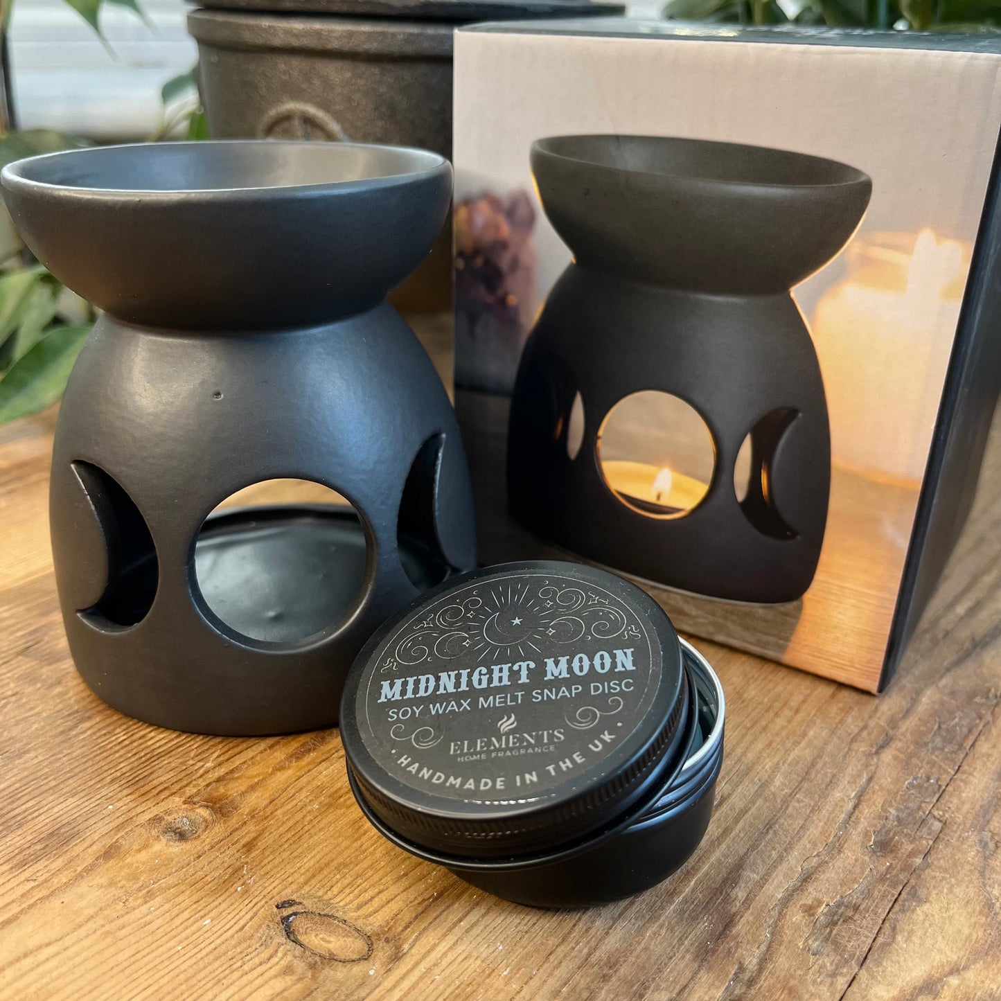 Black ceramic oil burner with a cutout triple moon design and a cool, matt finish. Pictured with a tin of wax melt snap discs