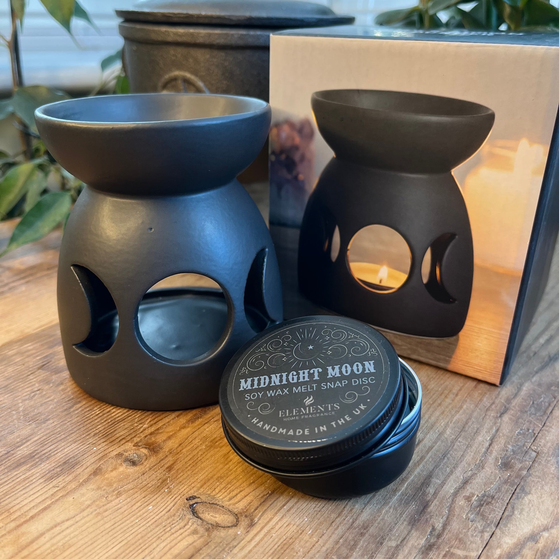 Black ceramic oil burner with a cutout triple moon design and a cool, matt finish. Pictured with a tin of wax melt snap discs