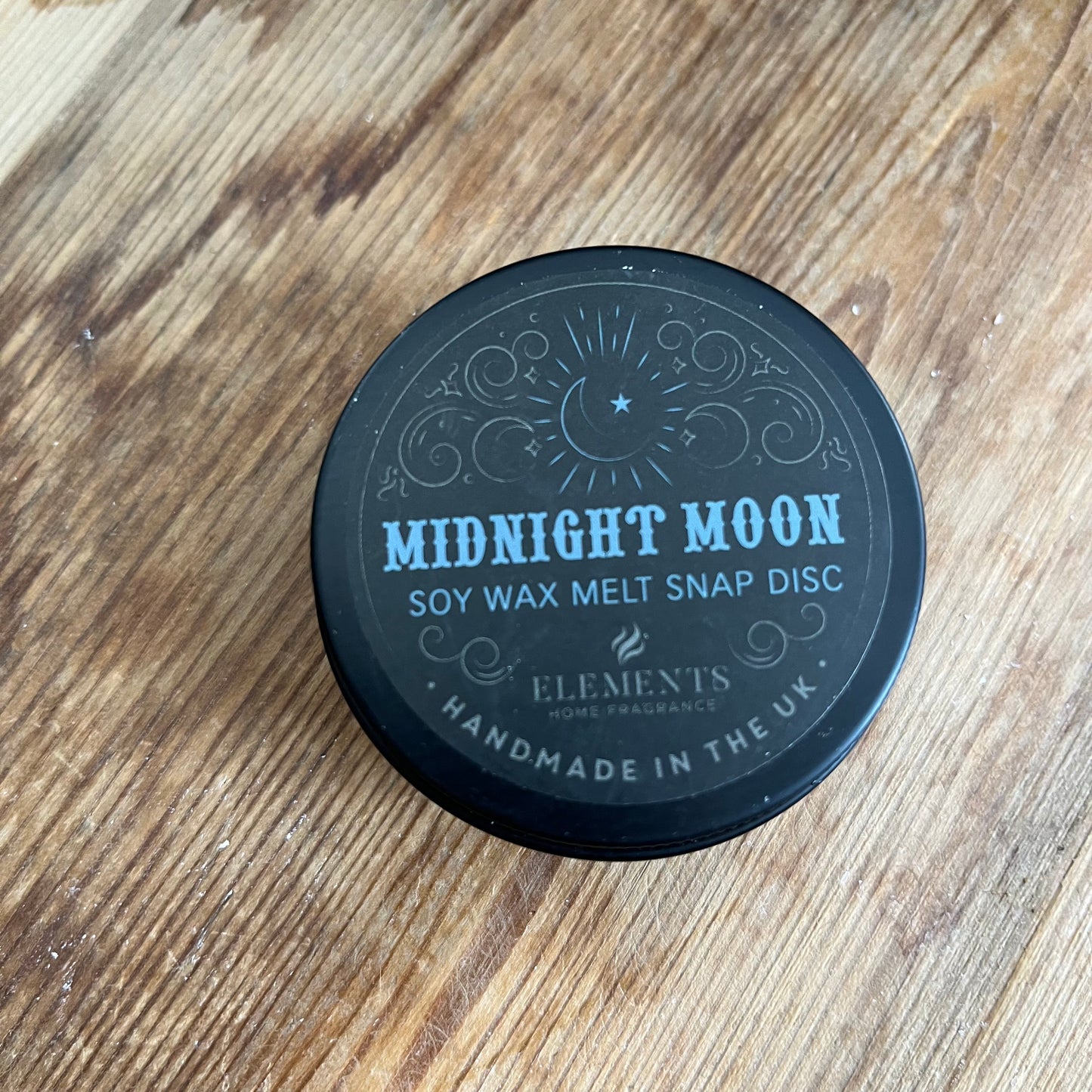 circular tin containing blue soy wax melt divided into 4. The lid of the tin reads midnight moon soy wax melt snap disc 