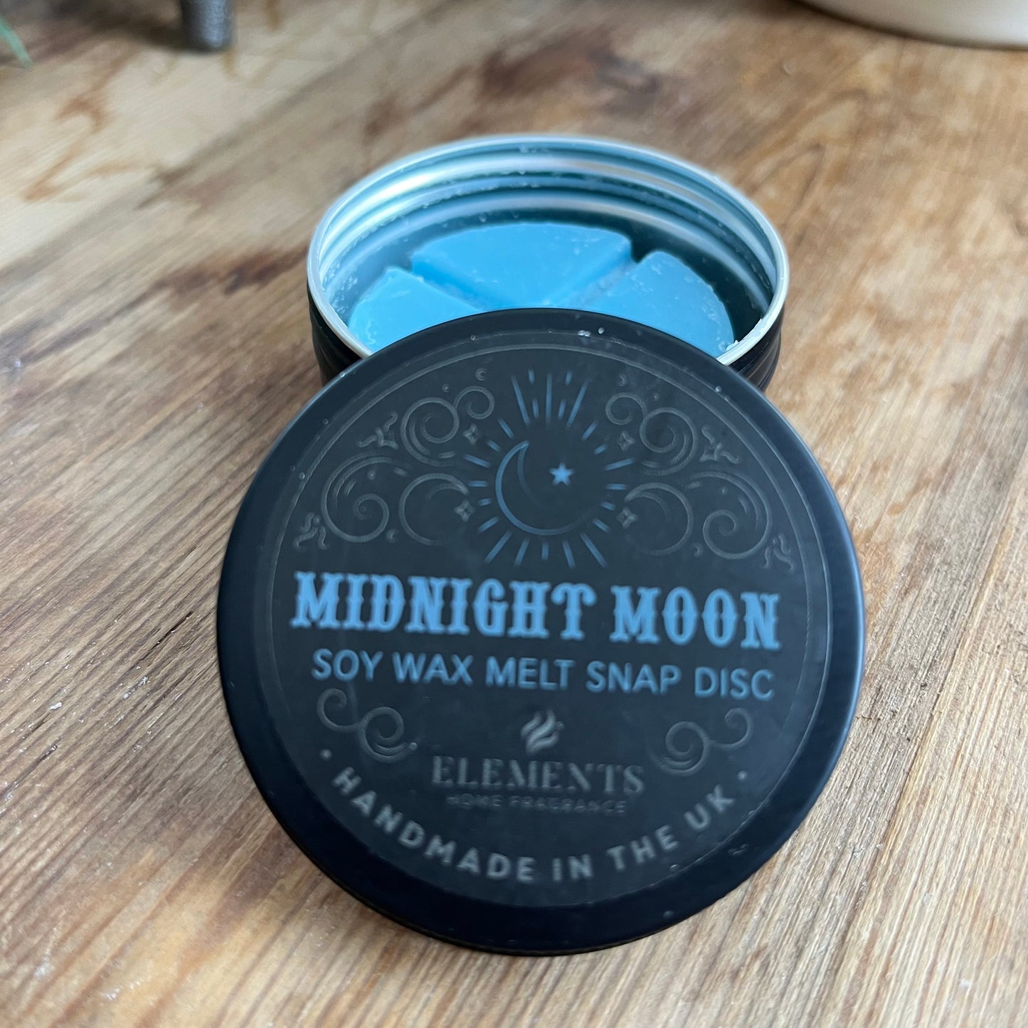 circular tin containing blue soy wax melt divided into 4. The lid of the tin reads midnight moon soy wax melt snap disc 