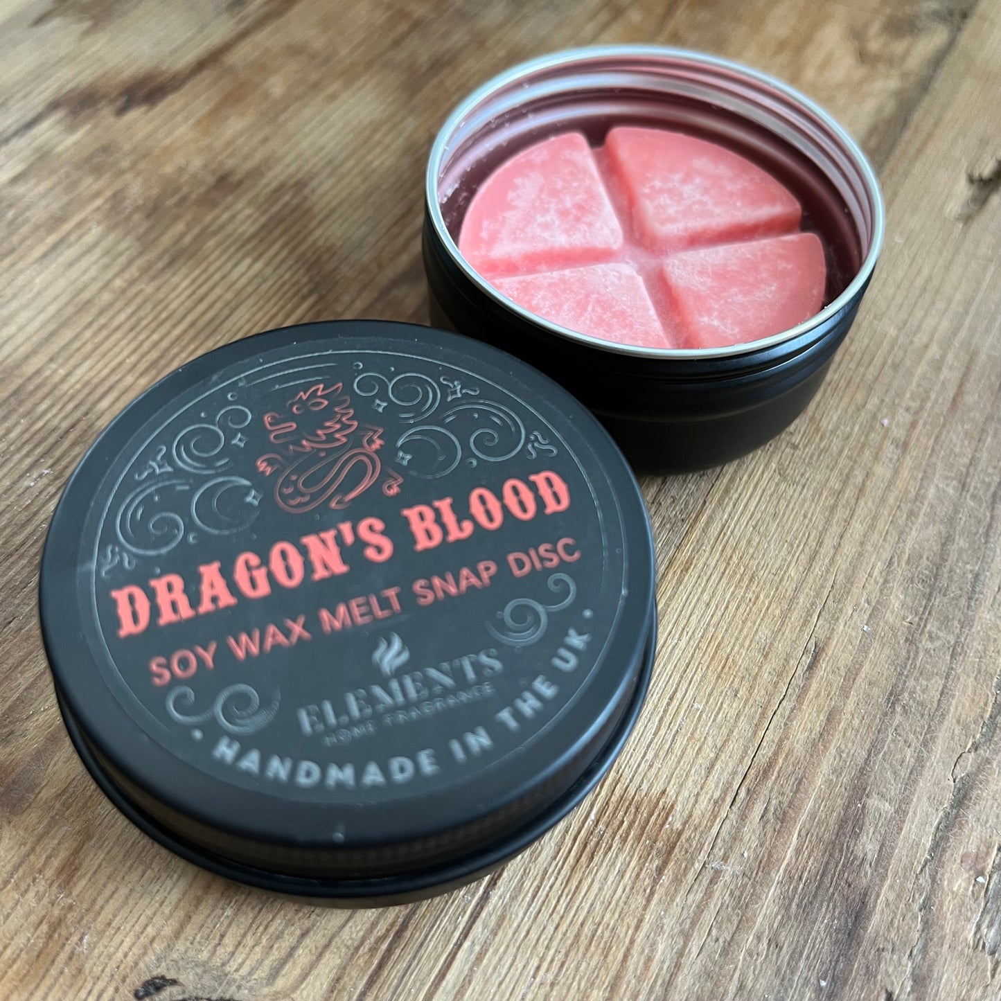 A circular tin containing a red wax melt divided into 4 sections. The tin lid reads Dragons blood soy wax melt snap disc 