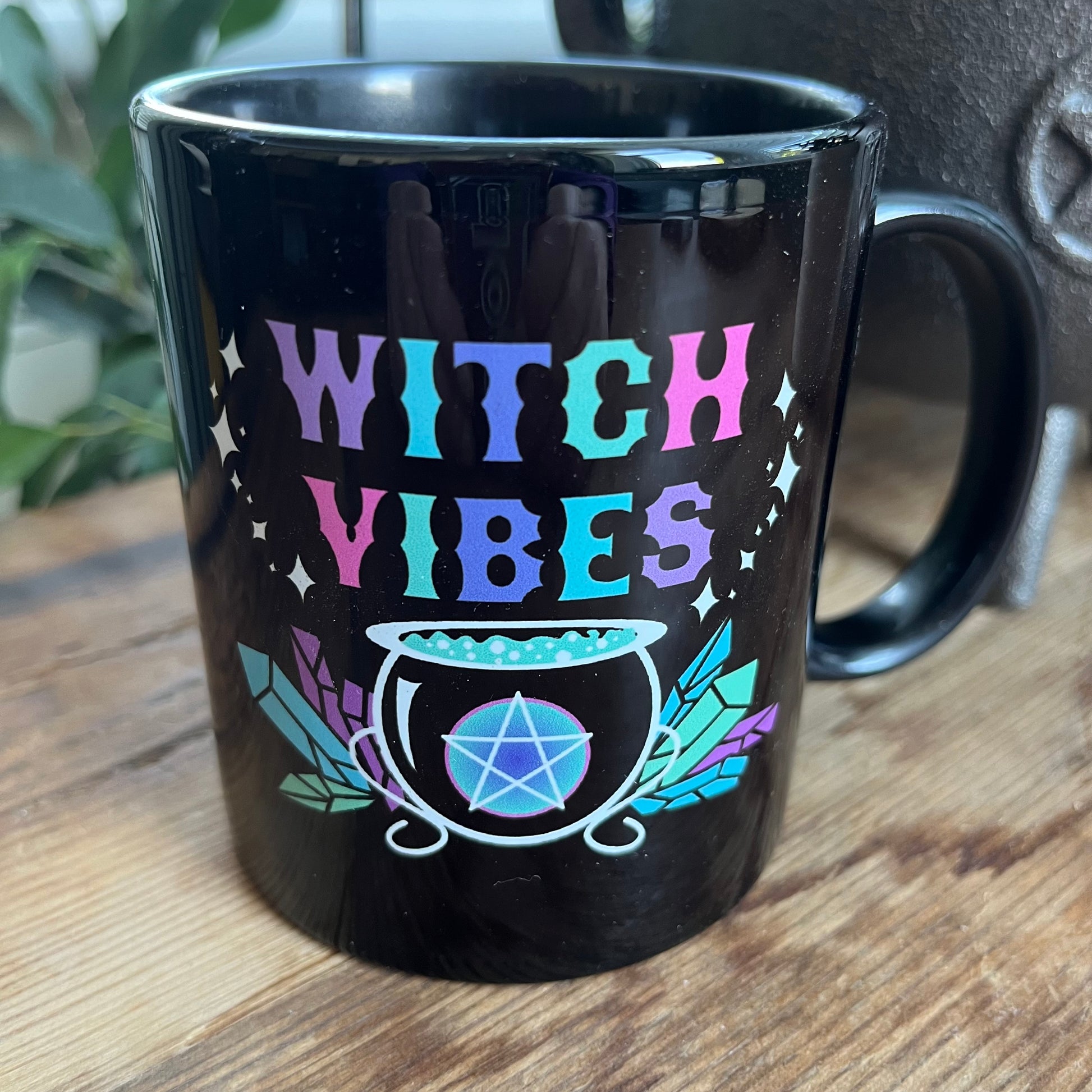 Black mug with the words witch vibes in colourful text and an illustration of a cauldron , crystals and pentagram 