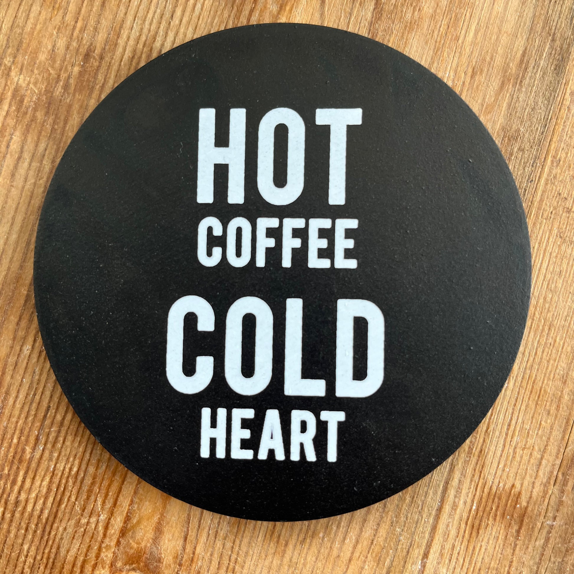 Black Coaster with the words Hot Coffee Cold Heart written boldly in white