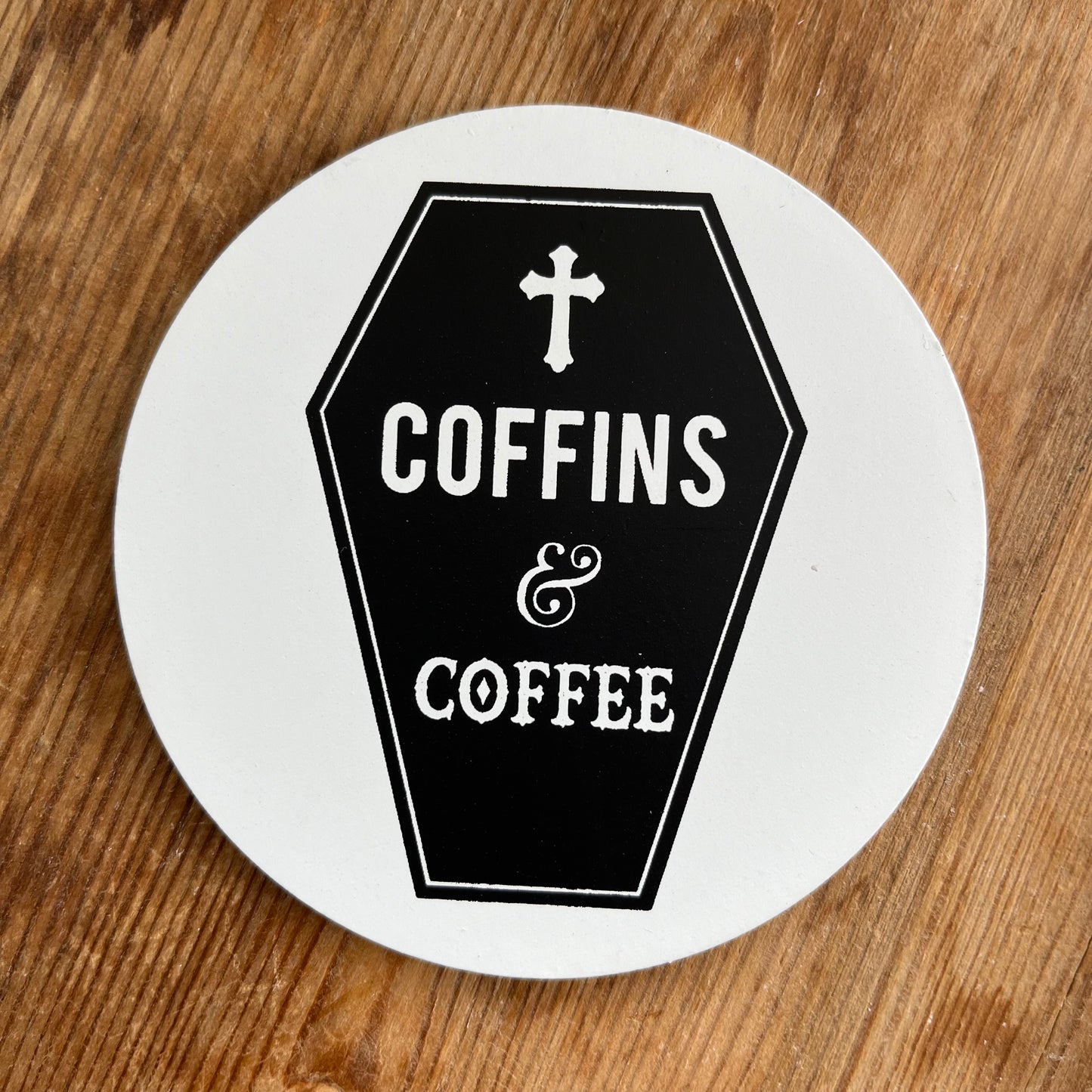 White Coaster featuring a Gothic Black coffin image and the words Coffins and coffee in bold white text