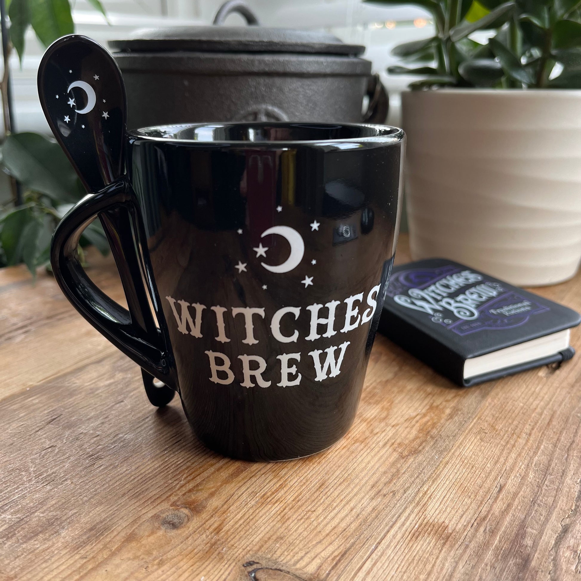 Black mug with the words Witches brew and a moon and star design in white. A matching spoon slots into the handle of the mug 