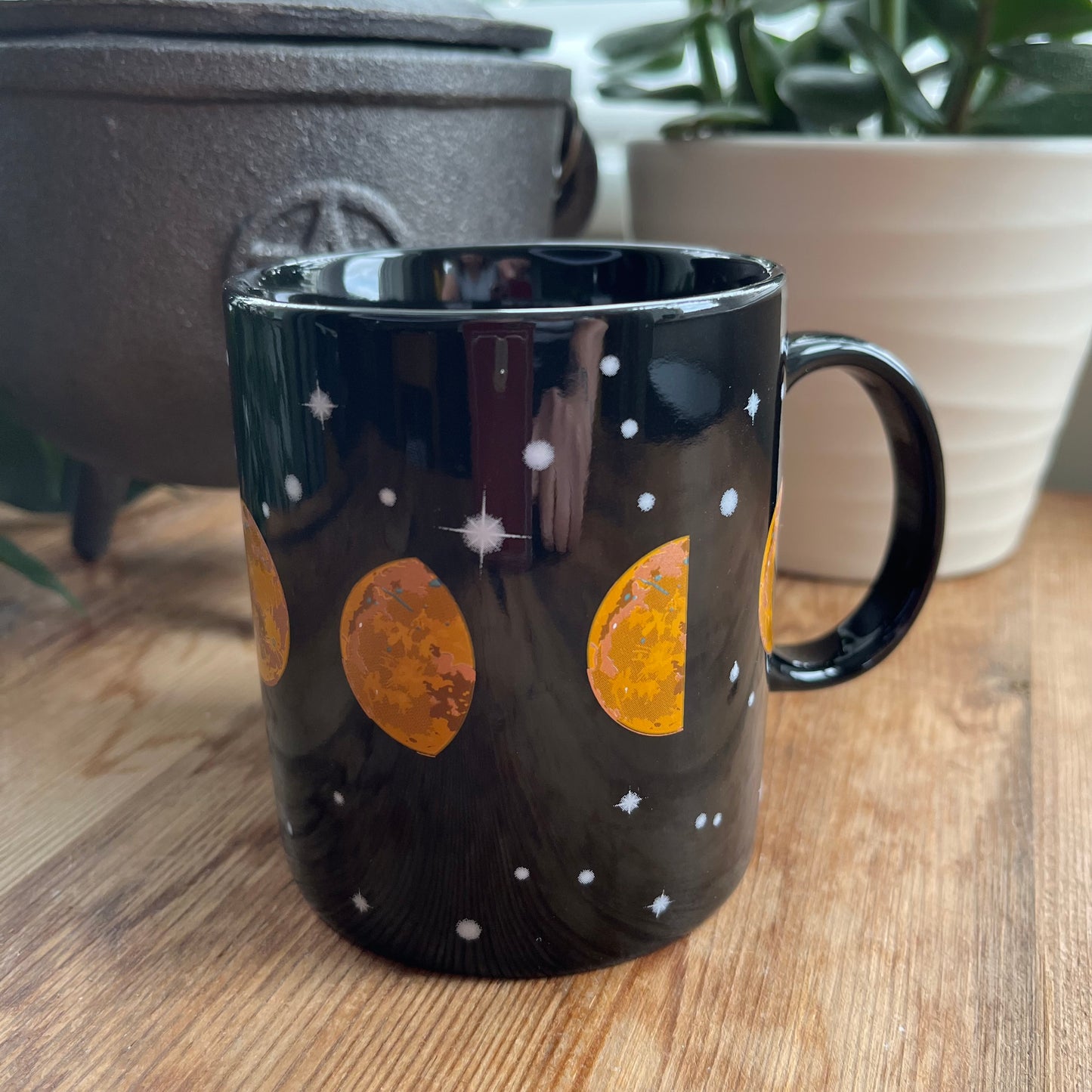 A Black mug featuring all of the moon phases around the mug 