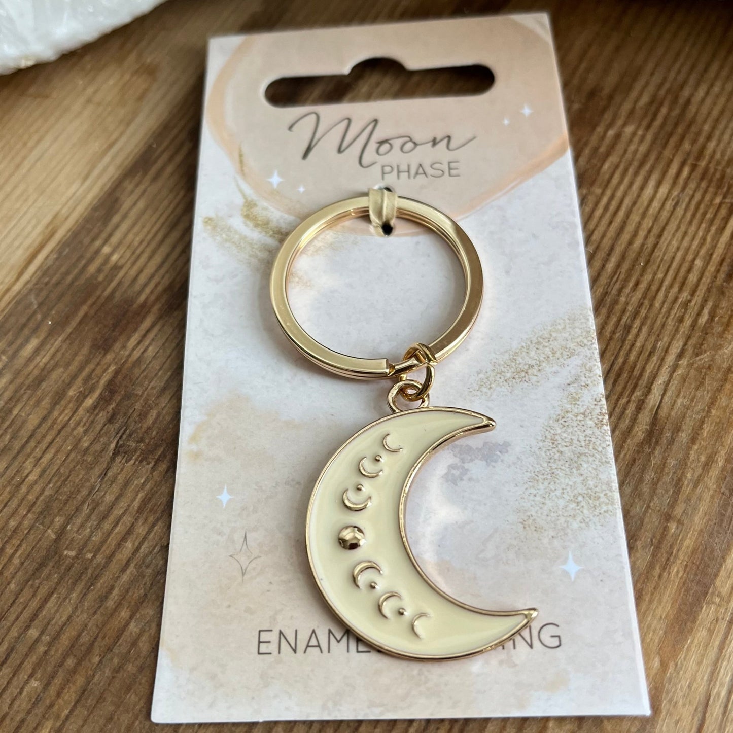 Cream Crescent moon enamel shape witch moon phases in gols shown along the crescent moon shape on a gold coloured key ring 