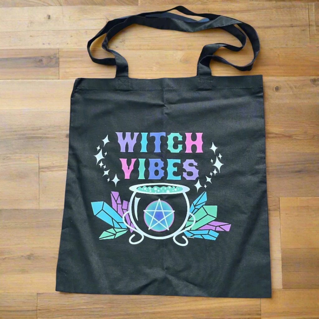 Black tote bag with 'WITCH VIBES' text and a graphic design featuring a cup, crystals, and a spell.