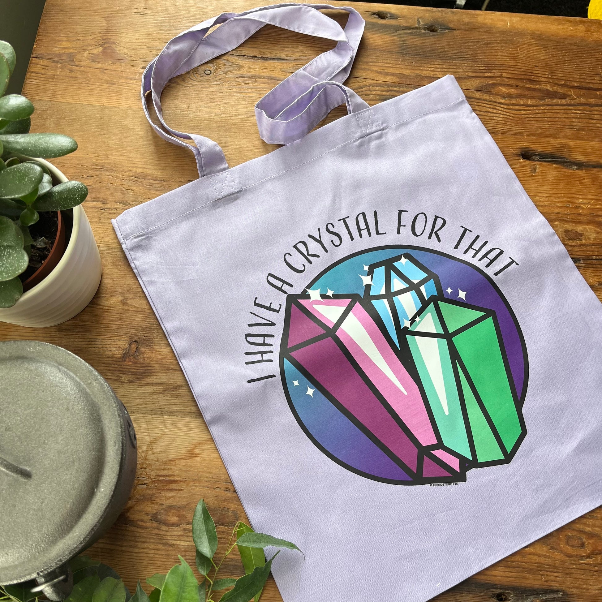 Tote bag with crystal design and text on a wooden surface with plants.
