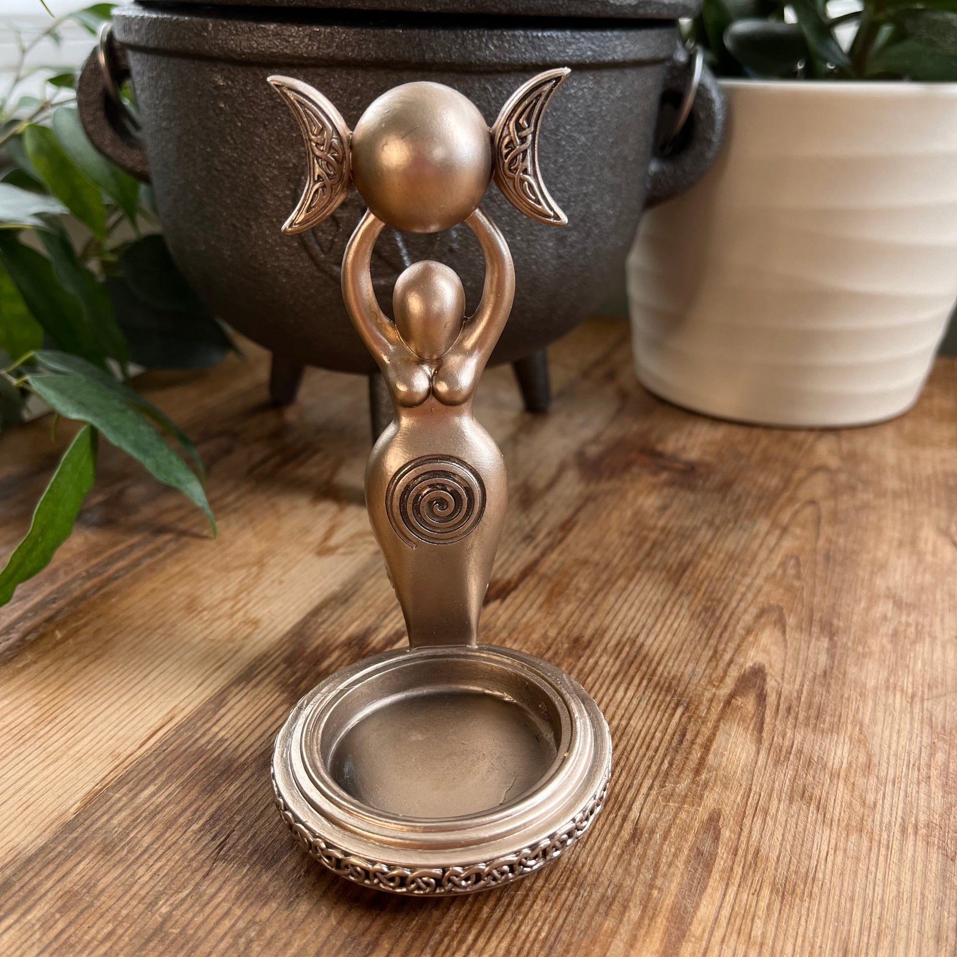 Bronze Spiral Goddess Tealight Holder. goddess stands on a round base with a tree outline emerging from her wide hips, She holds a triple moon above her head. 
The round base is  cut-out , to hold a tealights candle. Cast in resin with a stunning bronze finish,