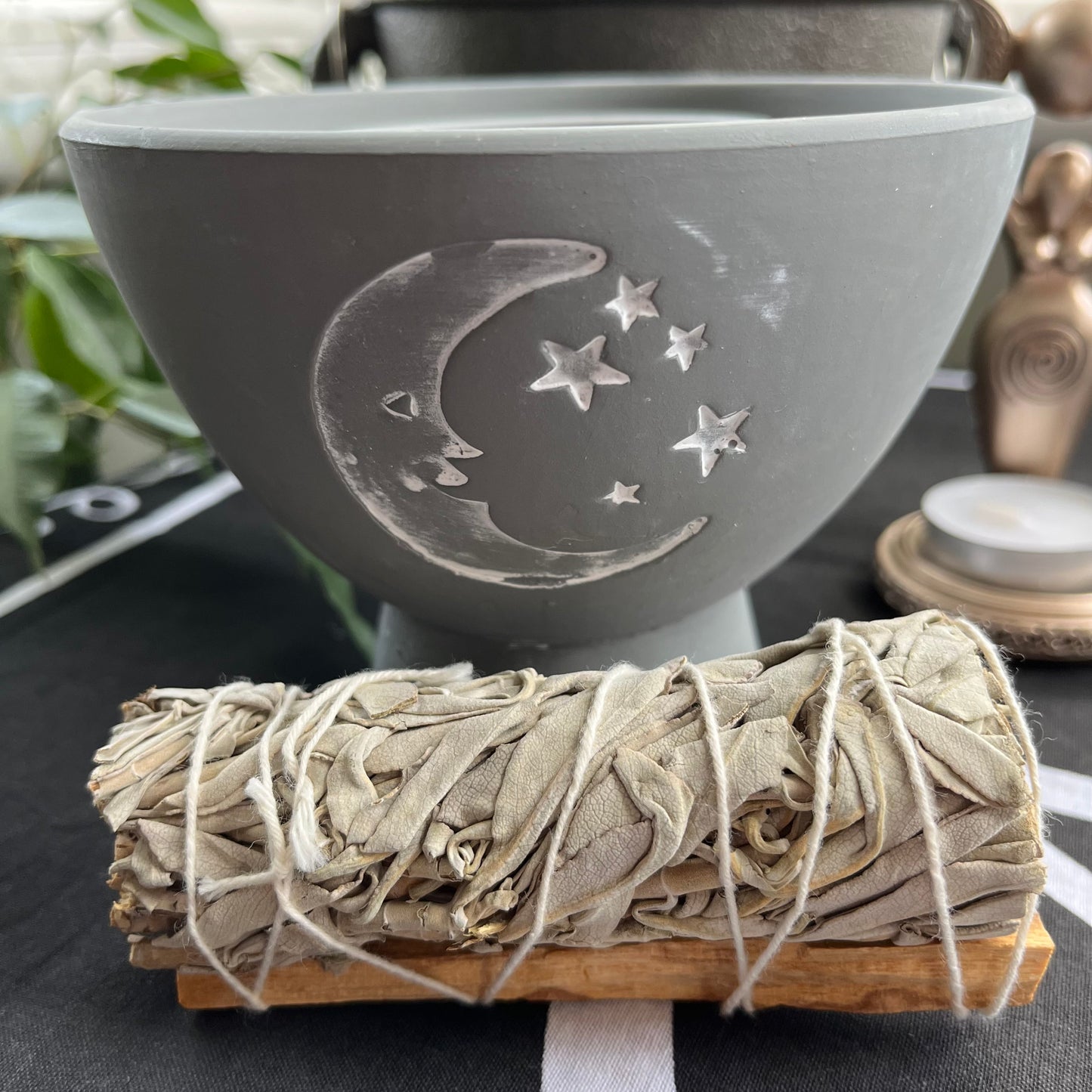 Grey rustic looking pot for holding herbs and smudge sticks while they burn. has a white painted motif of moon and stars on the side. Photographed on an Altar with a smudge stick 