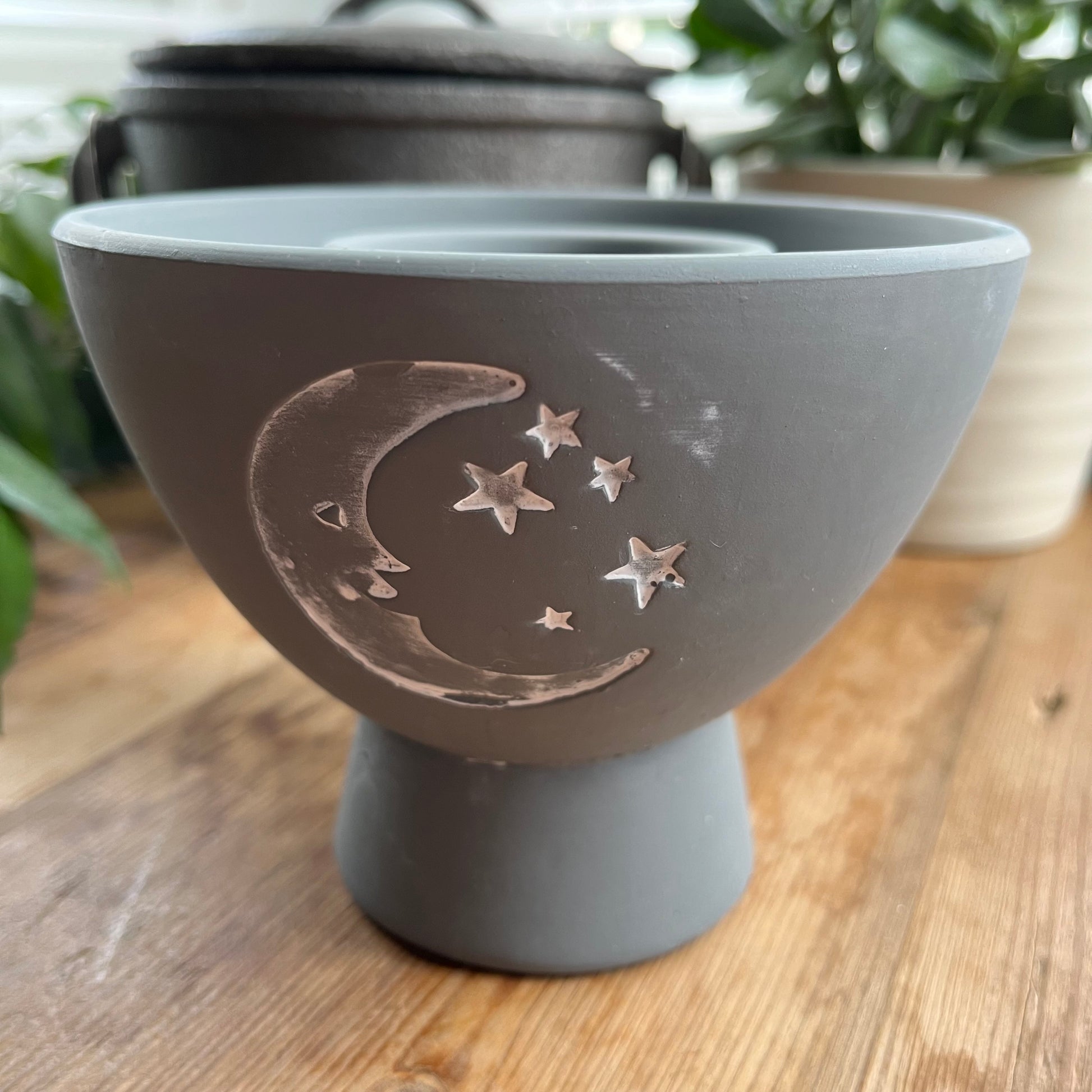 Grey rustic looking pot for holding herbs and smudge sticks while they burn. has a white painted motif of moon and stars on the side.