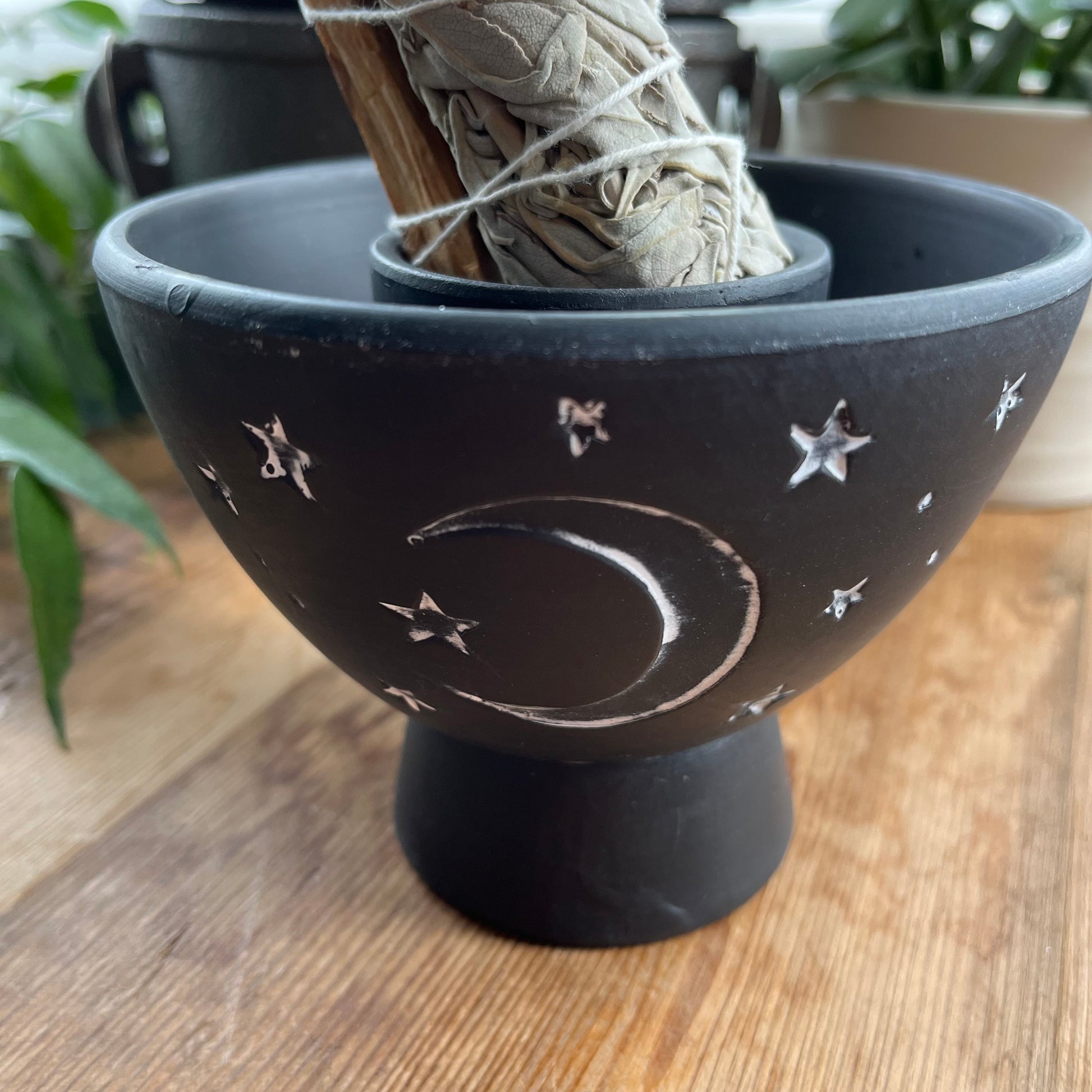 Rustic Black Terracota bowl designed to hold herbs and smudge sticks while burning. Has a white painted moon and stars motif on the side. Photographed with a smudge stick in the central  dipped area especially designed to hold smudge sticks upright 