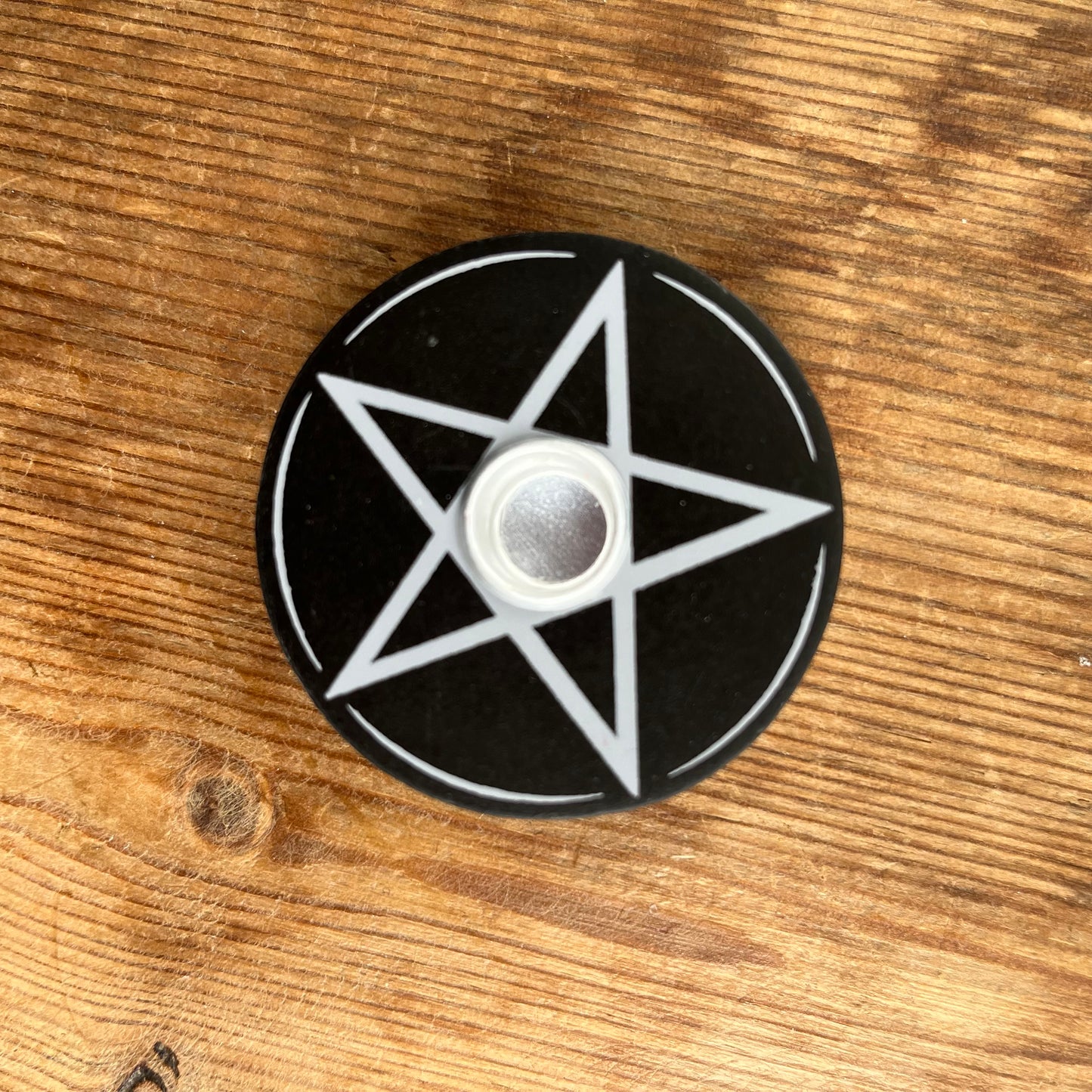 Circular black wooden candle holder with a white pentagram design on its surface designed to hold spell candles. 