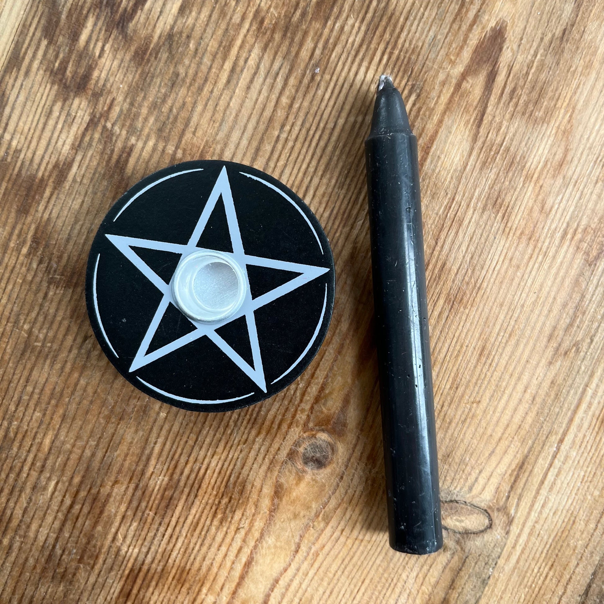 Circular black wooden candle holder with a white pentagram design on its surface designed to hold spell candles. 