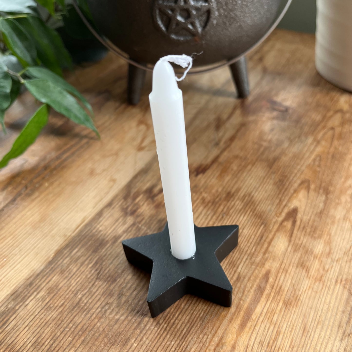 Black wooden candle spell holder in the shape of a star holding a white spell candle