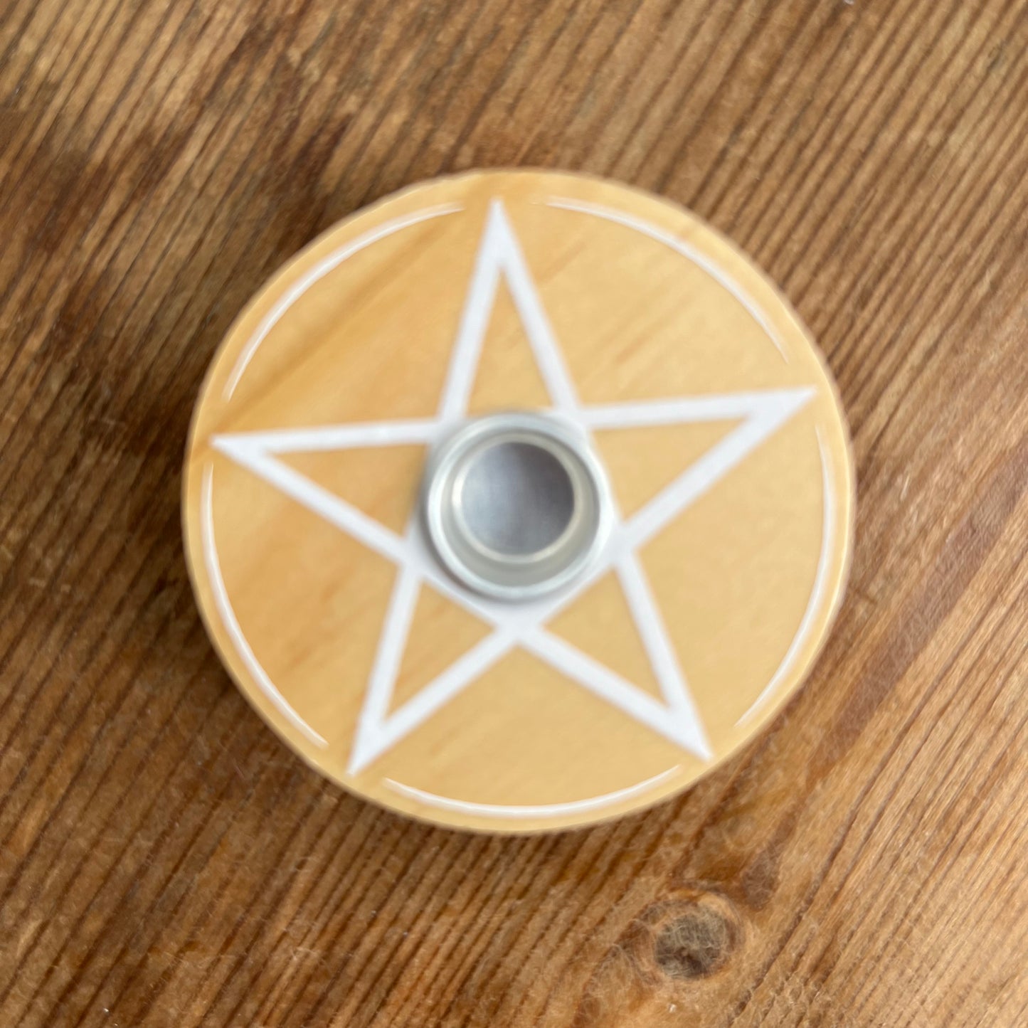 Natural wood circular spell candle holder with a white pentagram design on its surface 