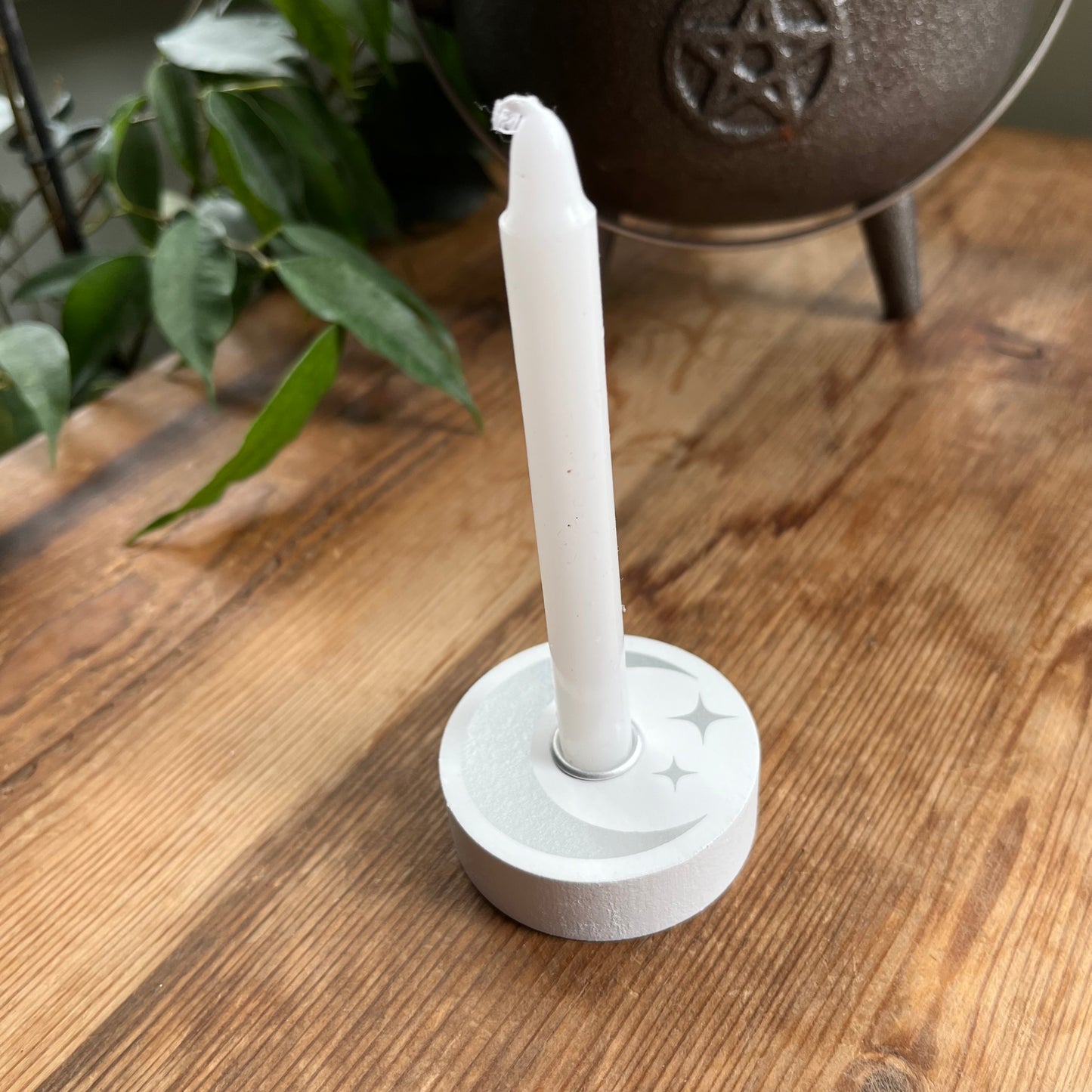 White circular wooden candle spell holder with a silver moon and star design on its surface , holding a white spell candle