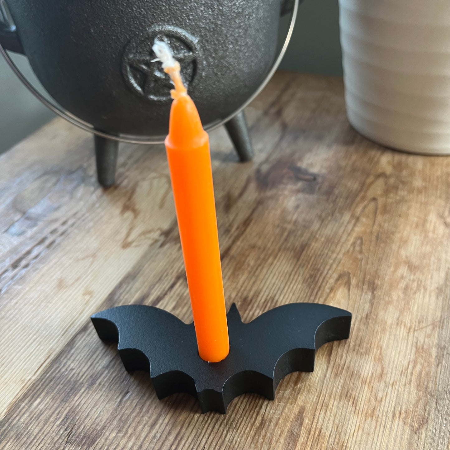 Black spell candle holder in the shape of a bat holding an orange spell candle