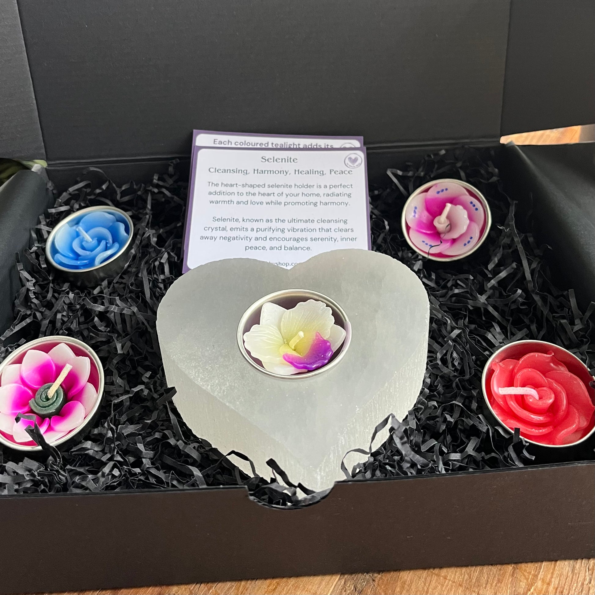 Chunky piece of natural selenite carved into a heart shape tealight holder. Alongside  collection of pretty coloured flower shaped tealights to use in the candle holder.  Presented in a black gift box. Also included are some cards explaining the metaphysical properties of selenite and colour associations. 