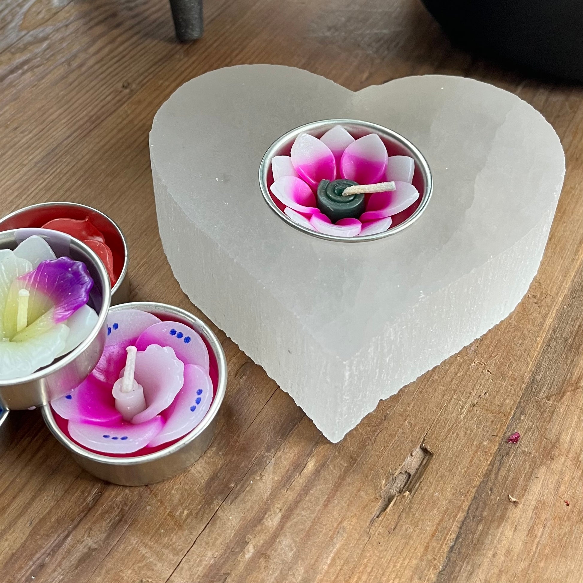 Chunky piece of natural selenite carved into a heart shape tealight holder. Alongside  collection of pretty coloured flower shaped tealights to use in the candle holder.  