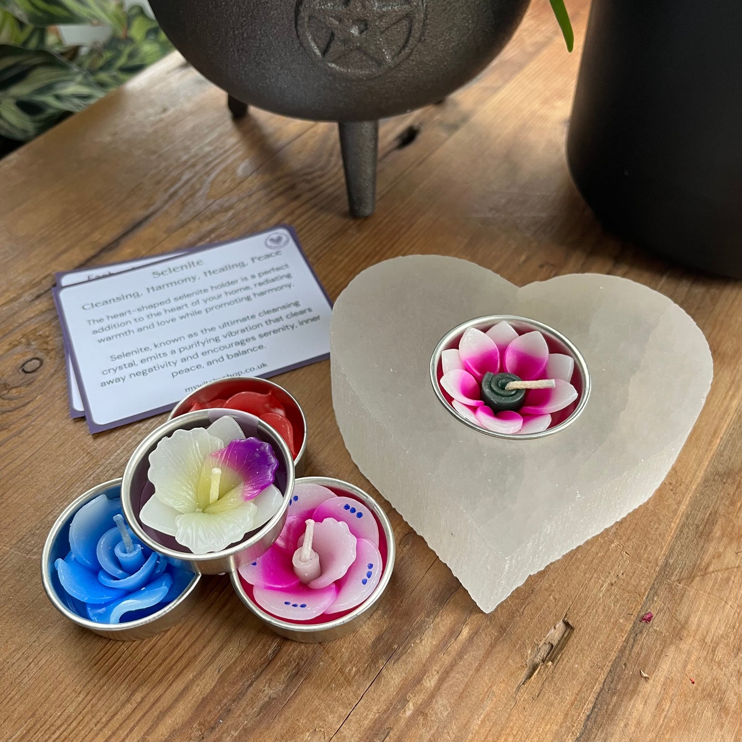 Chunky piece of natural selenite carved into a heart shape tealight holder. Alongside  collection of pretty coloured flower shaped tealights to use in the candle holder. 