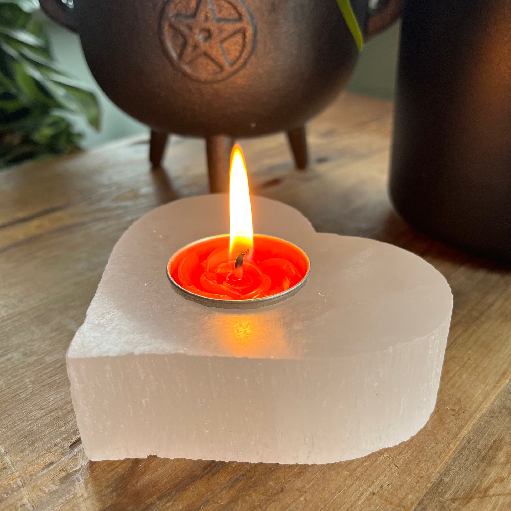 Chunky selenite carved heart shaped tealight holder looking warm and cosy with a lit red tealight candle. 