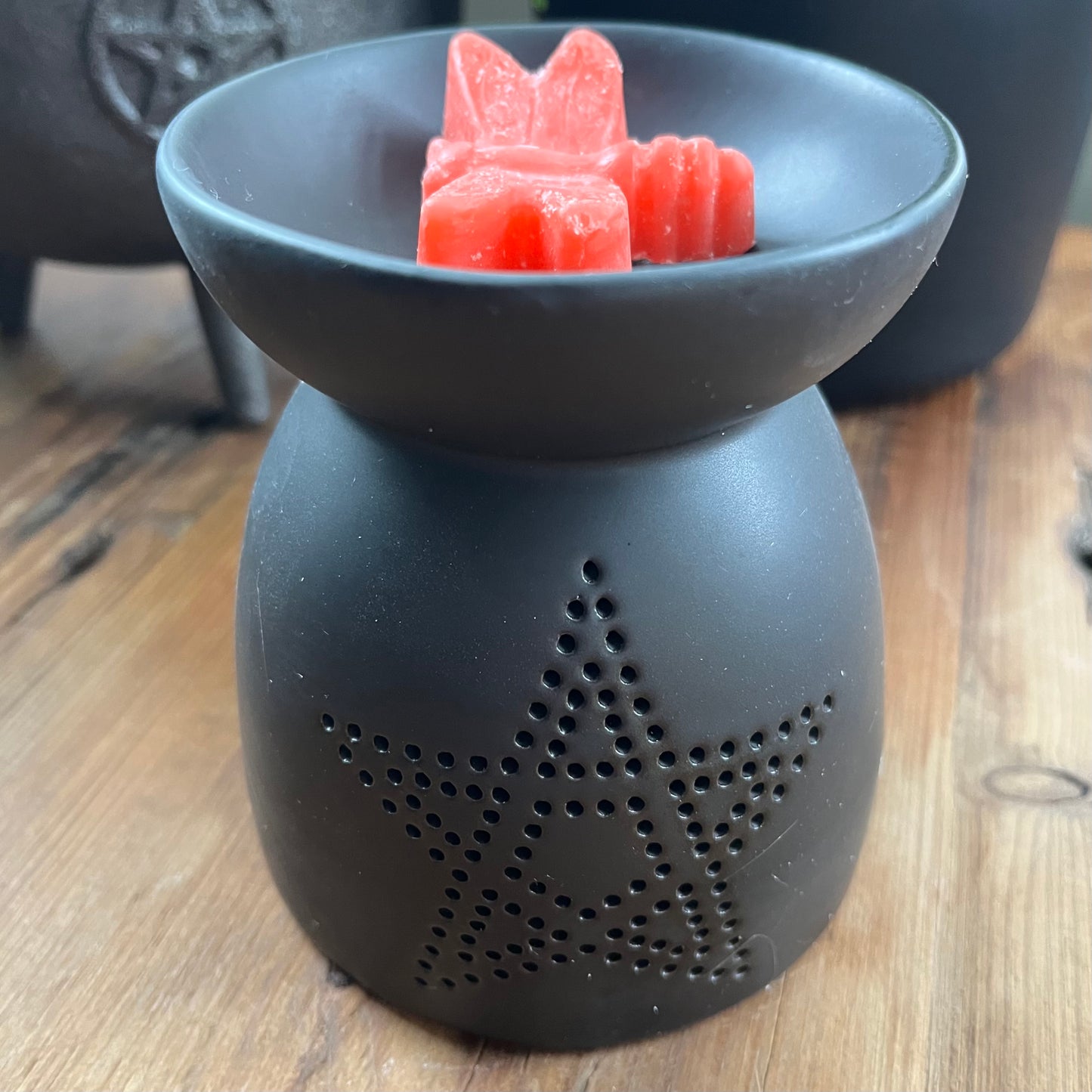 Black ceramic oil burner, featuring a pentagram cutout design and a smooth matte finish. Pictured with dragon fly wax melt and cauldron in the ackground.
