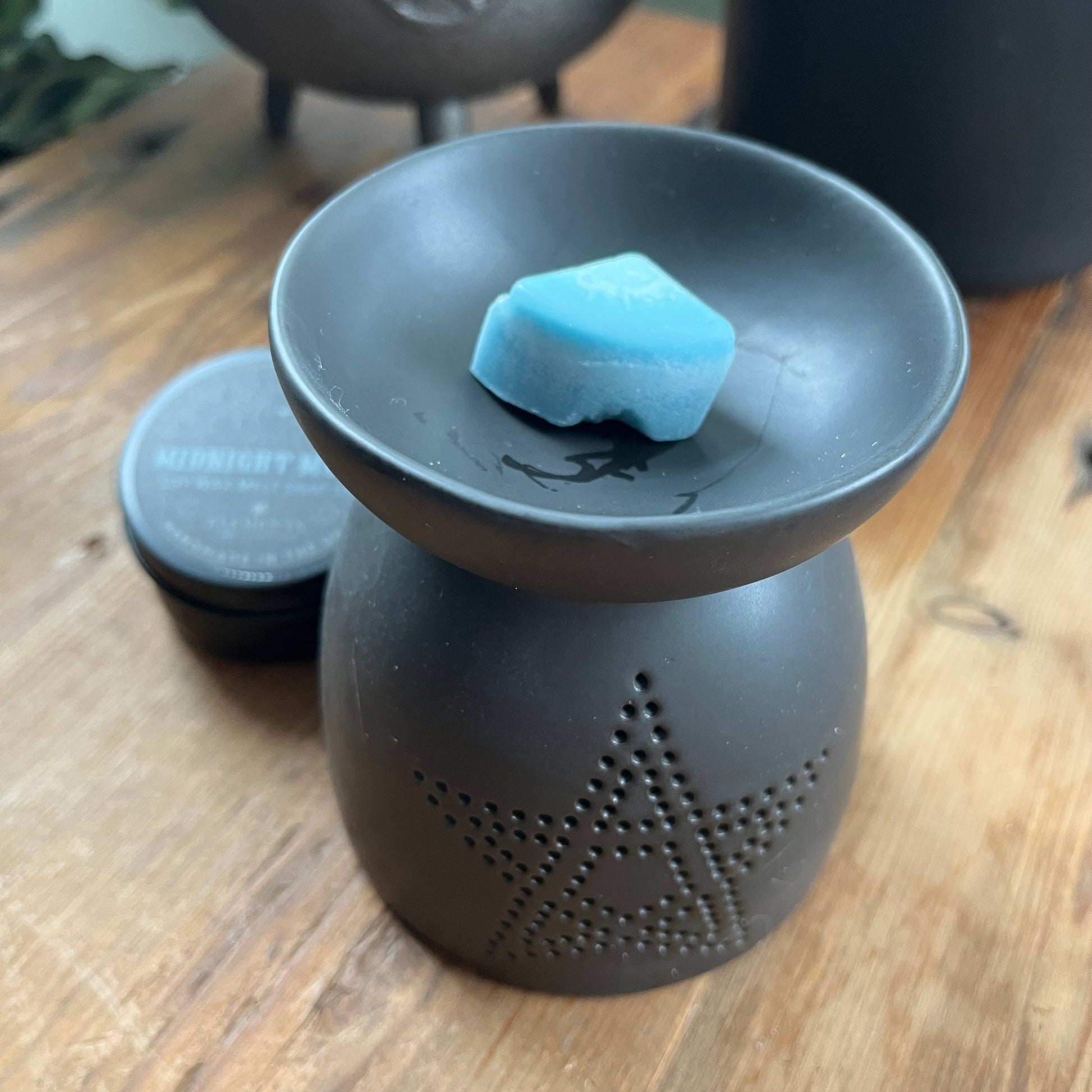 Black ceramic oil burner, featuring a pentagram cutout design and a smooth matte finish. Pictured with midnight moon wax melts. 