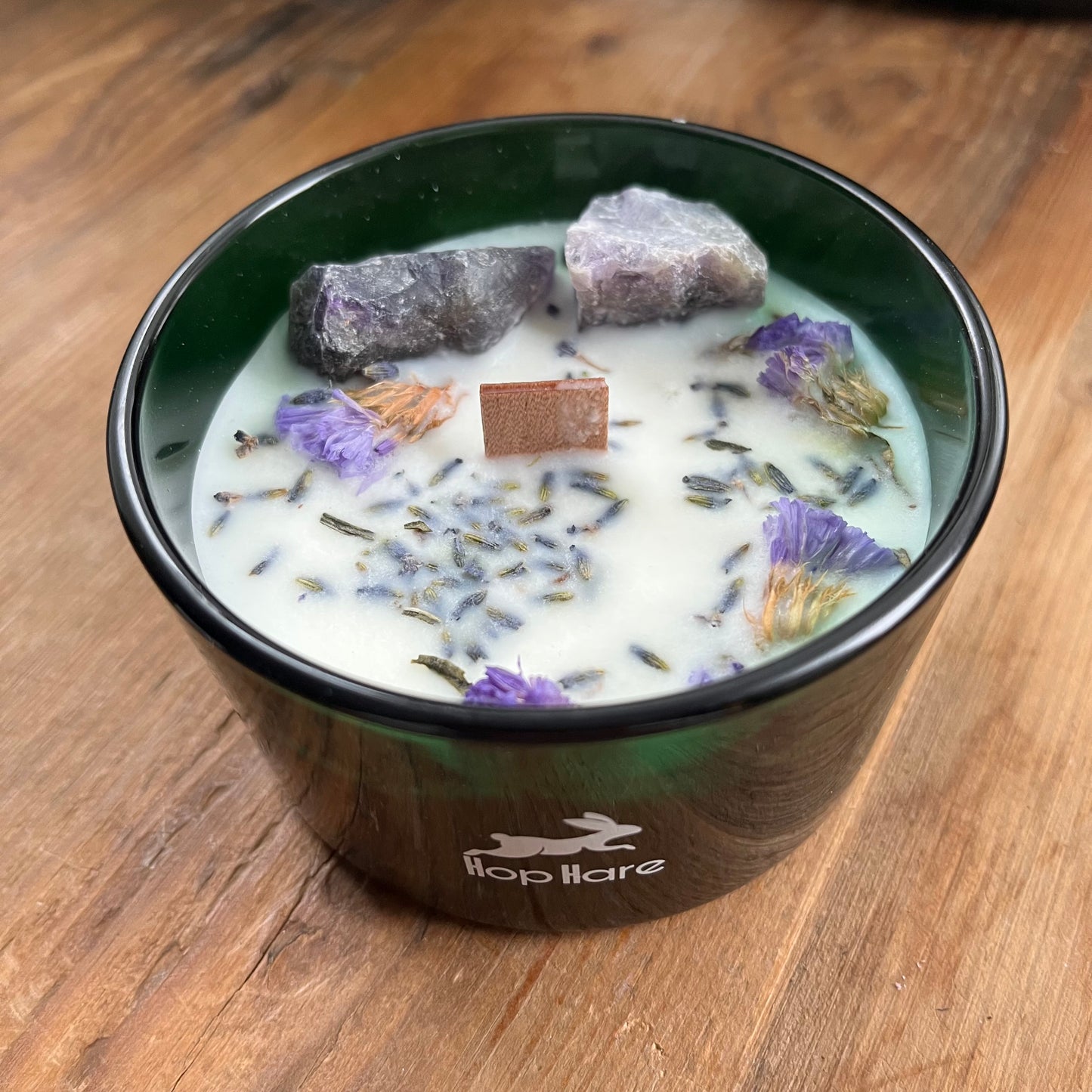 The top of the hop hare moon candle shows a wooden wick, large amethyst crystals and lavender flowers 