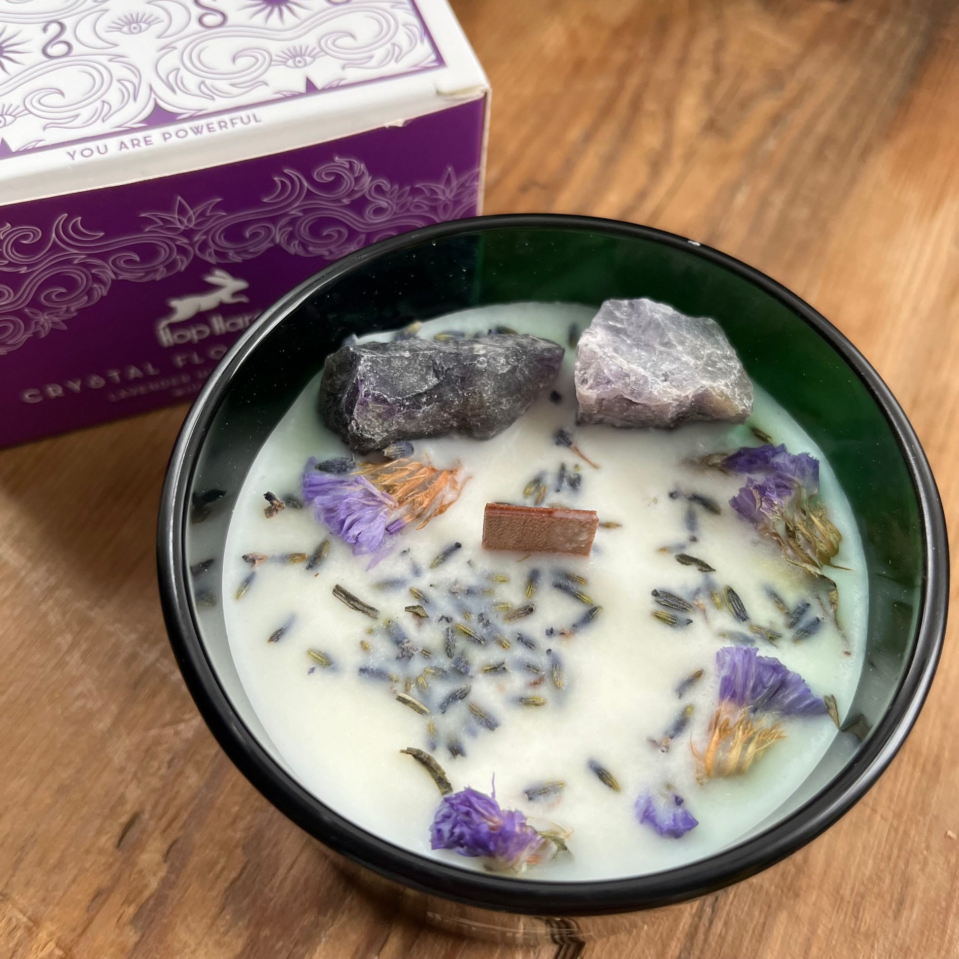 The top of the hop hare moon candle shows a wooden wick, large amethyst crystals and lavender flowers 