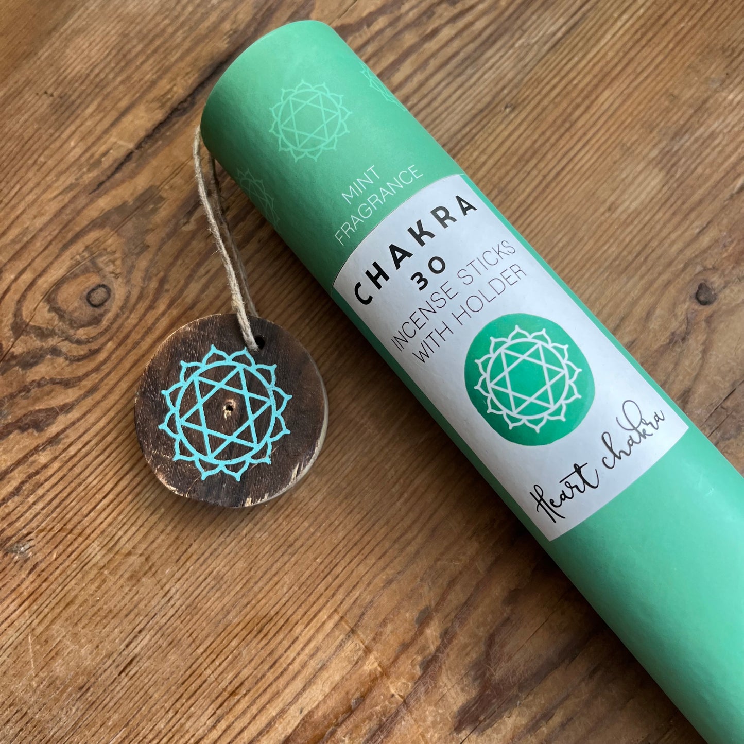 Green cardboard tube containg 30 sticks of mint scented incense for the Heart Chakra, with a wooden incense holder printed with the symbol for the Heart Chakra 