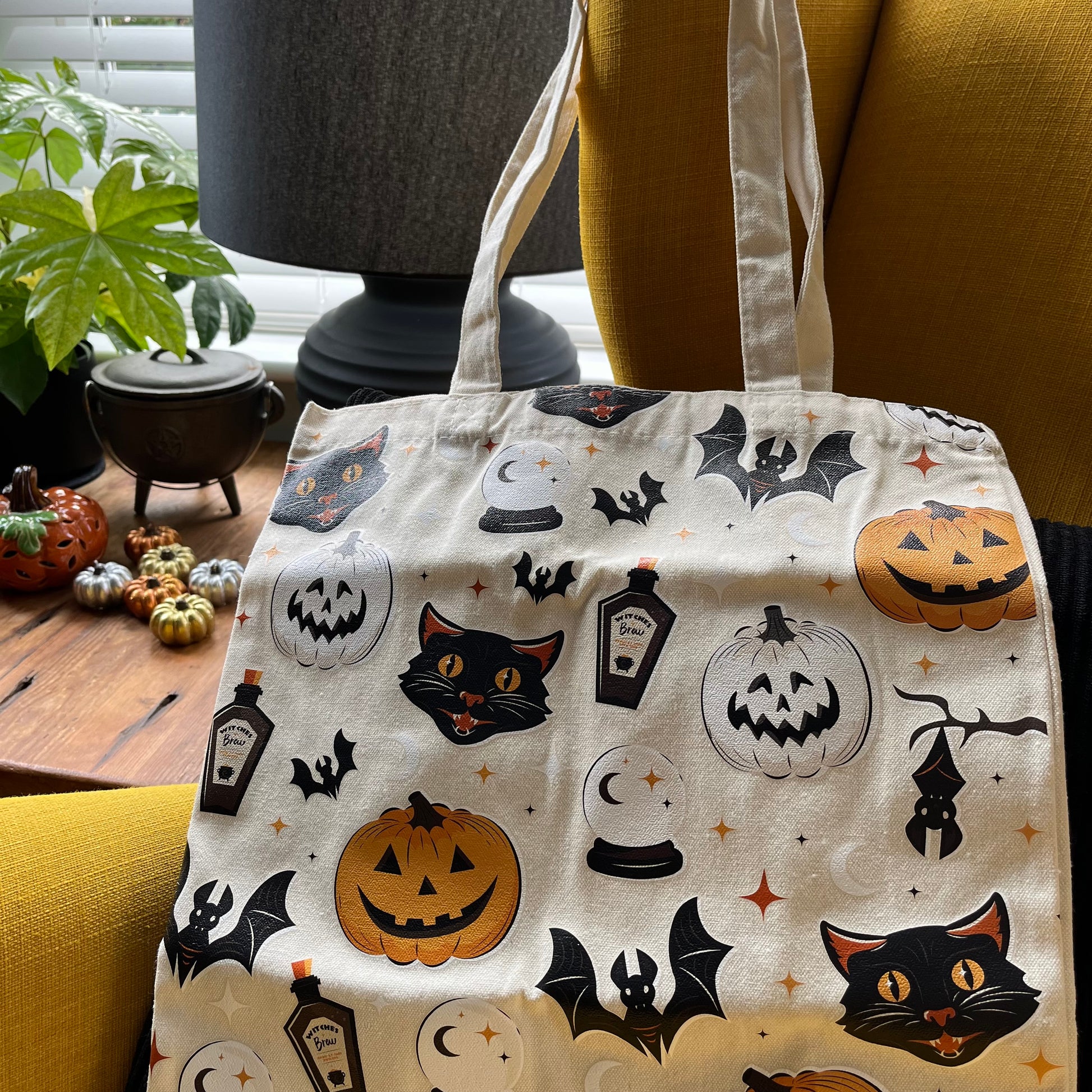 Tote bag with Halloween-themed design featuring pumpkins, cats, and bats on a neutral background.