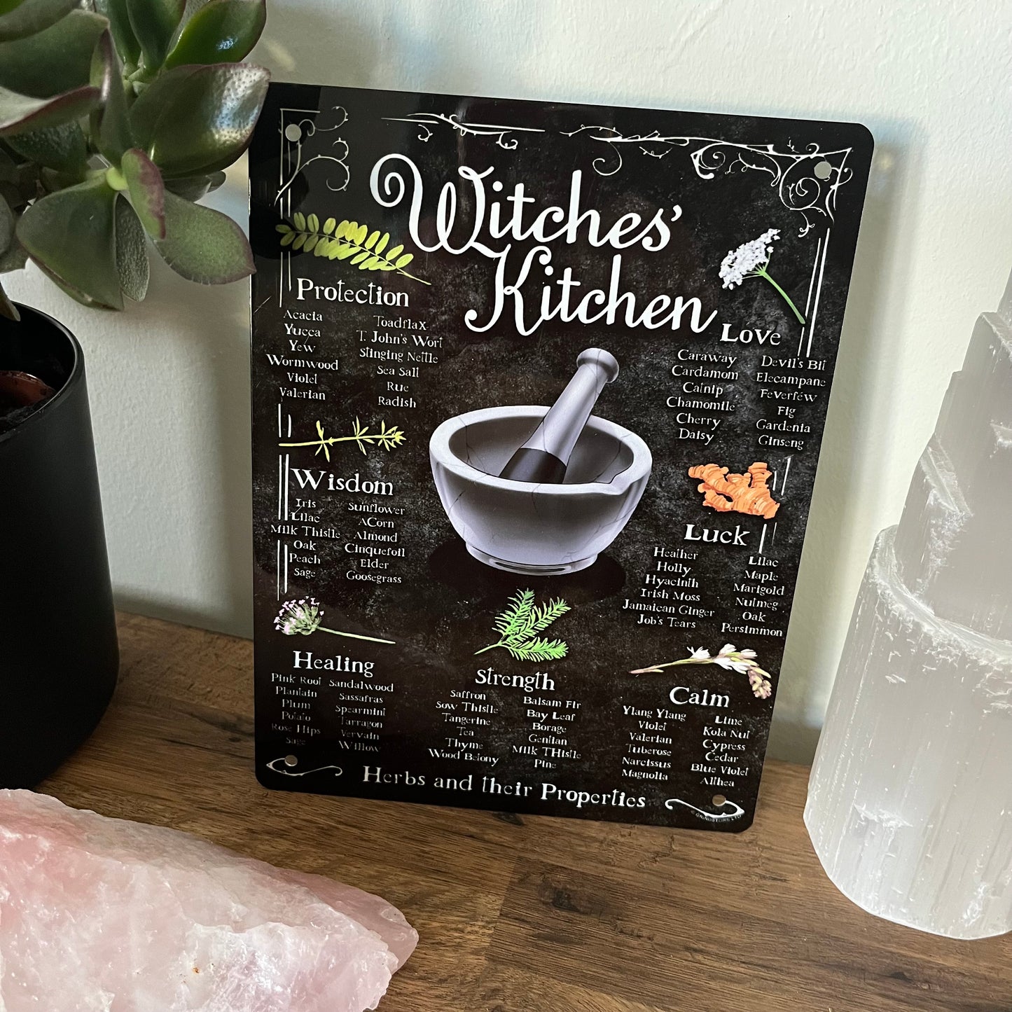 Decorative sign titled 'Witches' Kitchen' with various virtues and herbs on a wooden surface.