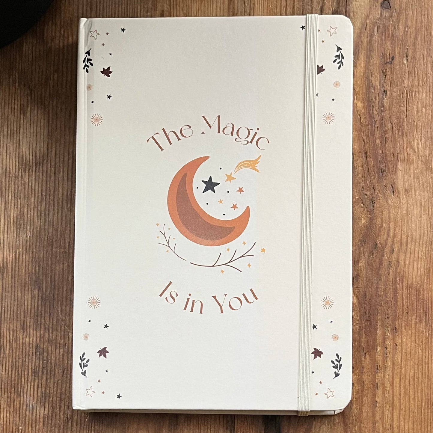 Notebook with 'The Magic is in You' design on a wooden surface