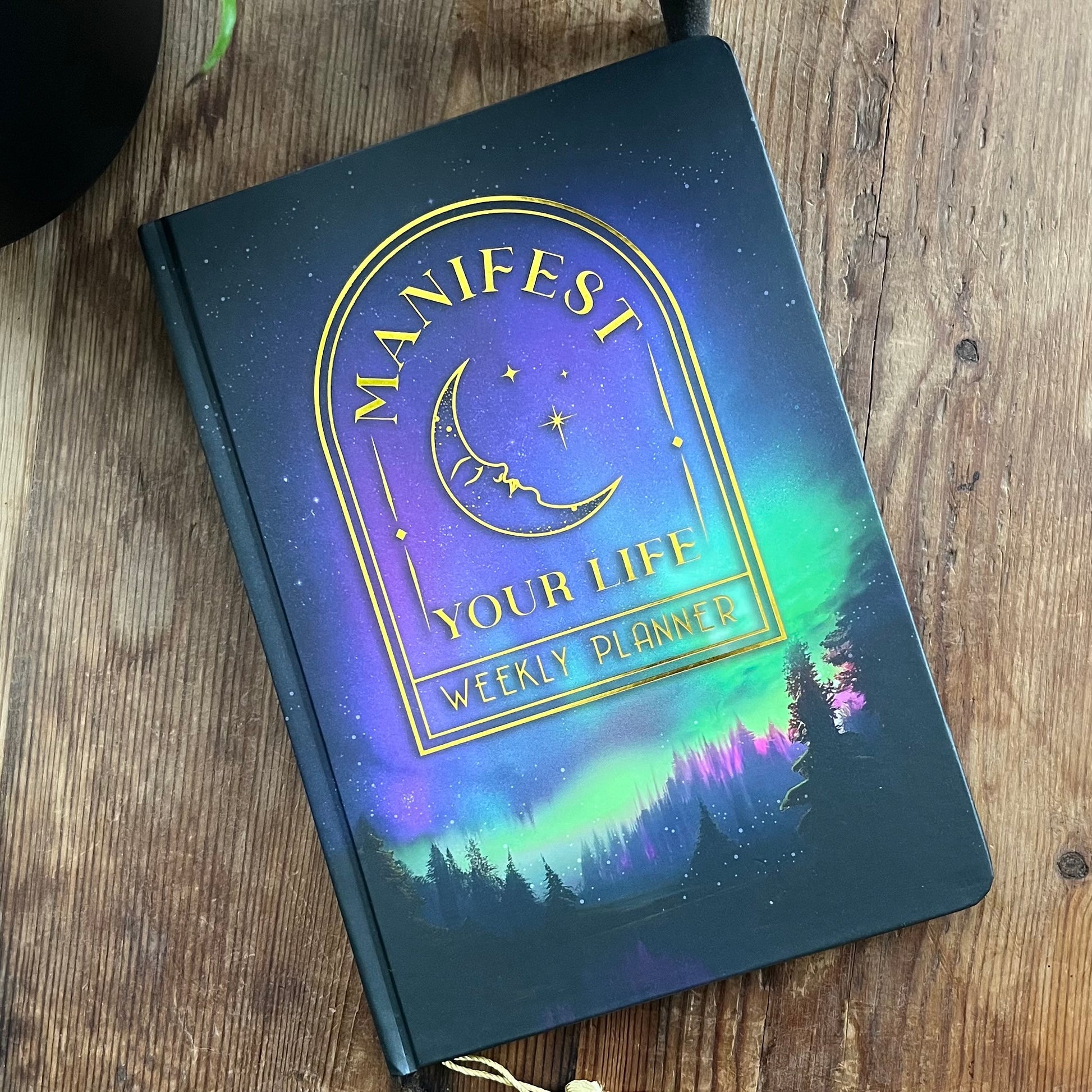 Weekly planner with 'Manifest Your Life' design on a wooden surface