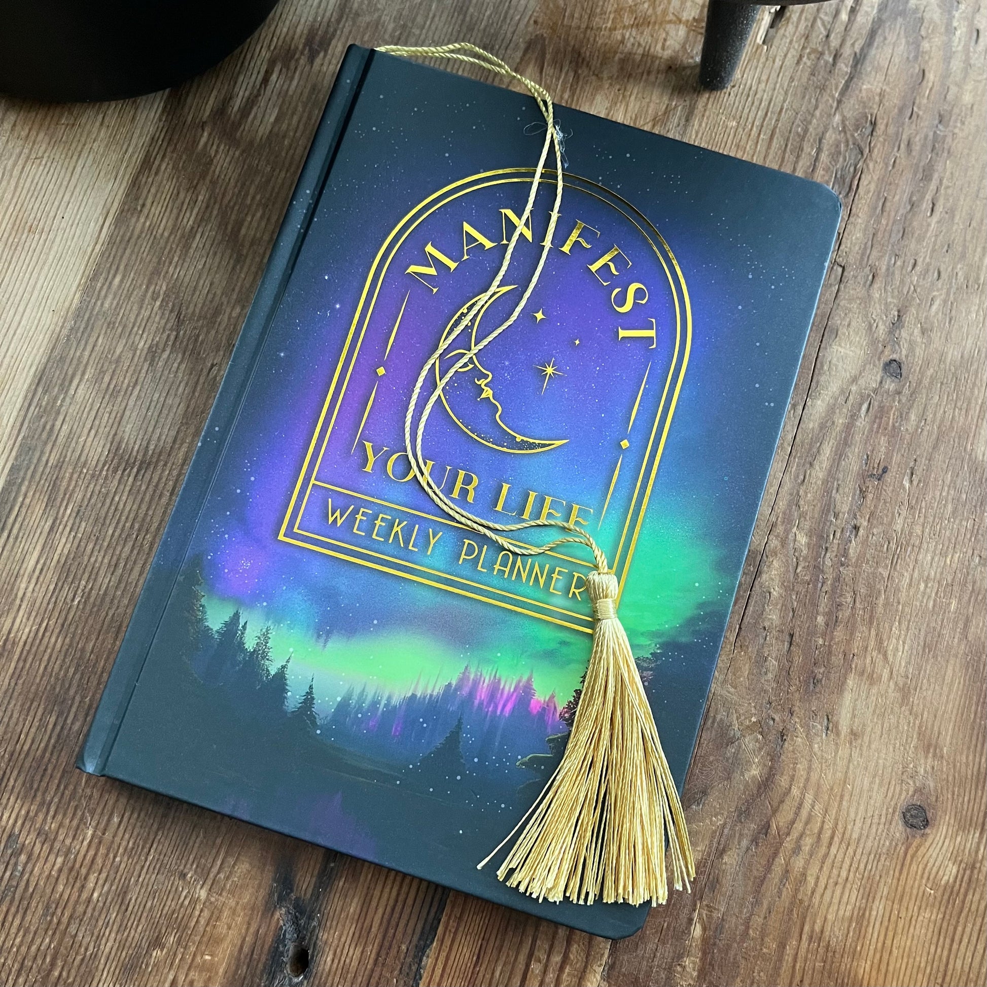 Weekly planner with 'Manifest Your Life' design on a wooden surface