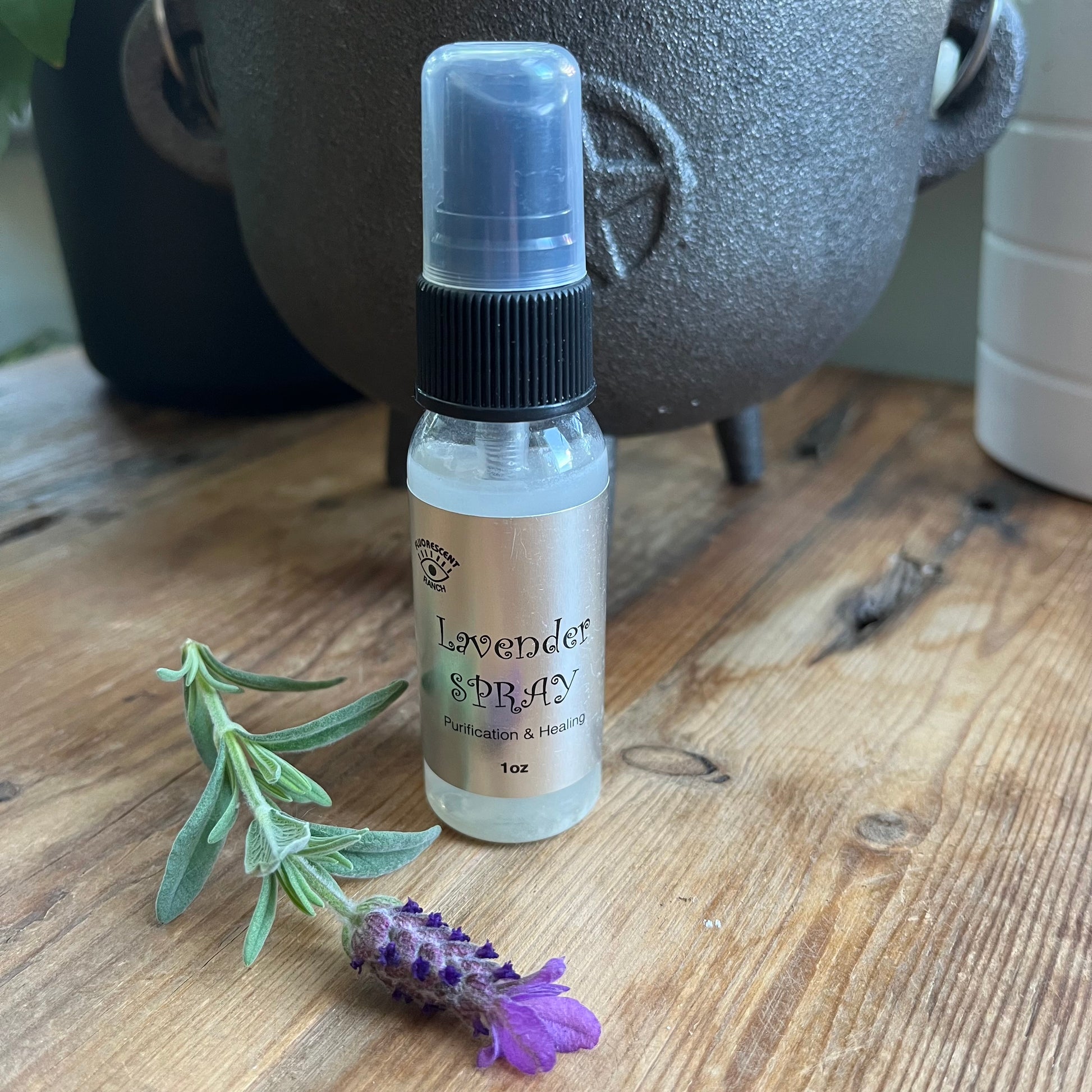 Lavender room spray in a clear glass spray bottle pictured with a sprig of Lavender 