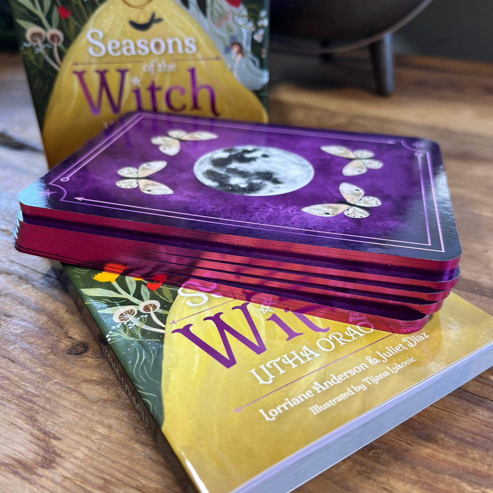 Stack of Purple coloured oracle cards on a wooden surface with 'seasons of a witch' oracle box
