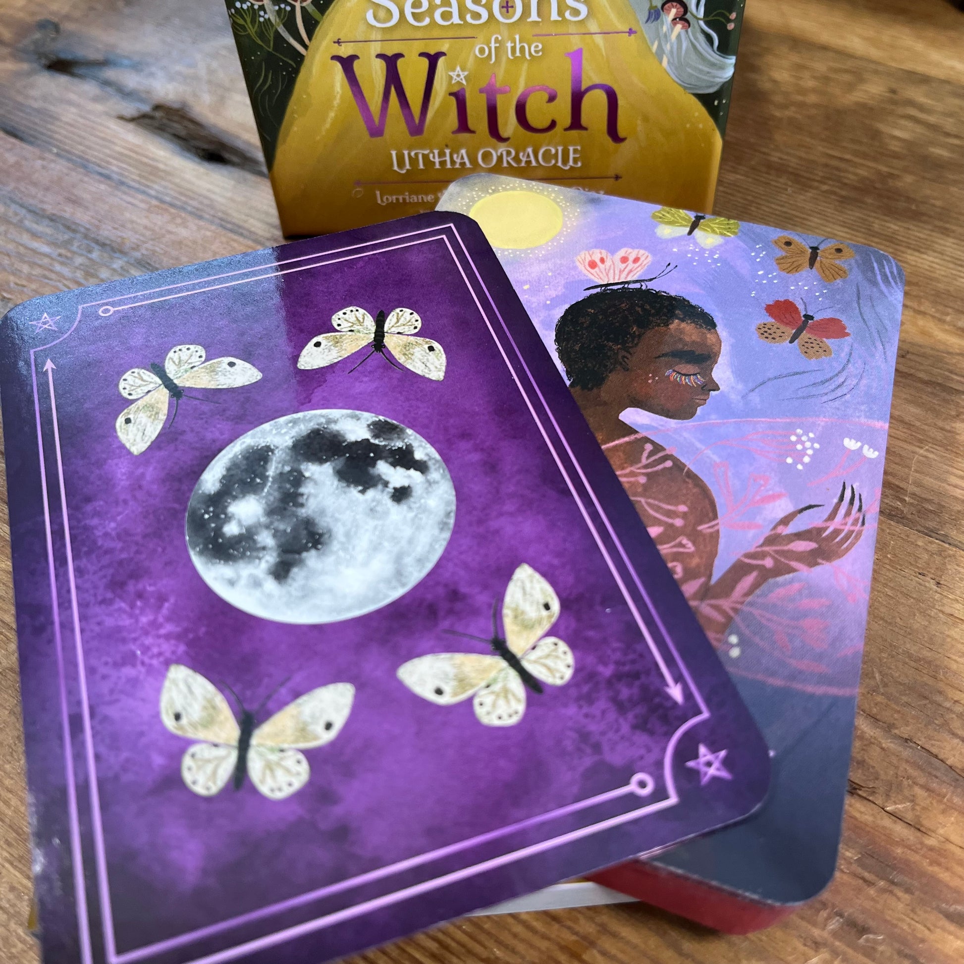 Oracle cards with a purple background featuring butterflies and a moon, on a wooden surface.