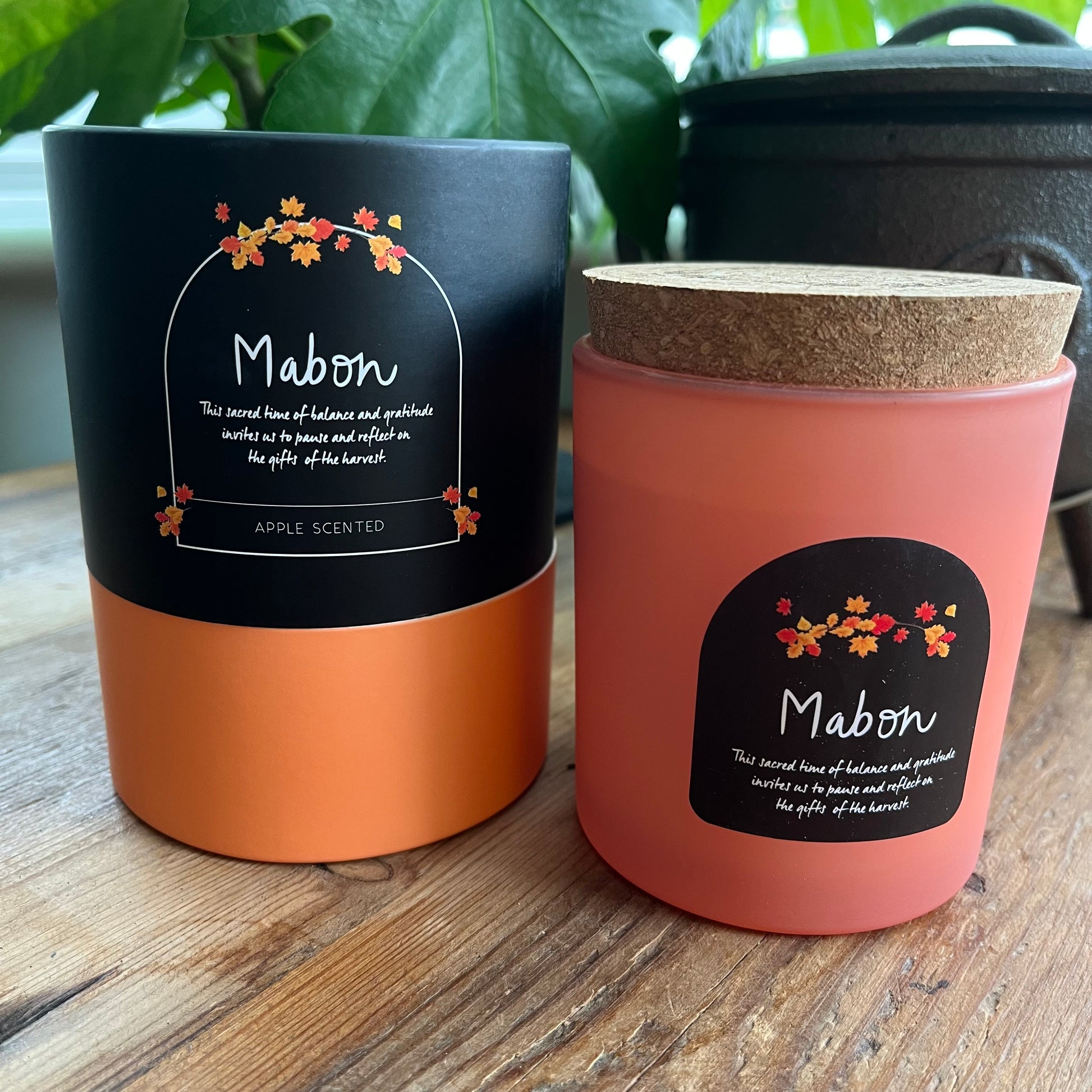 Two Mabon-themed candles on a wooden surface with plants in the background