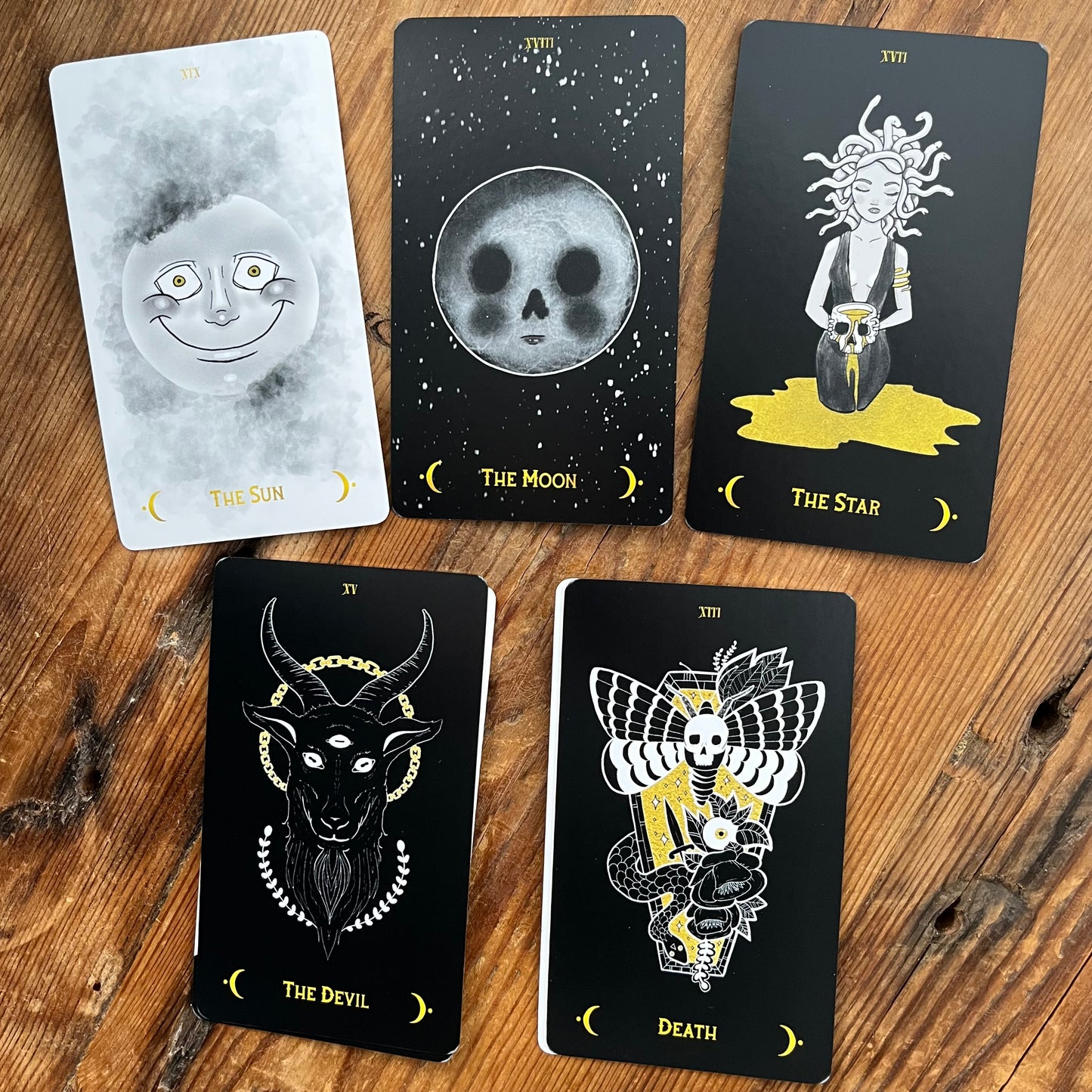 Five tarot cards with black and white illustrations on a wooden surface
