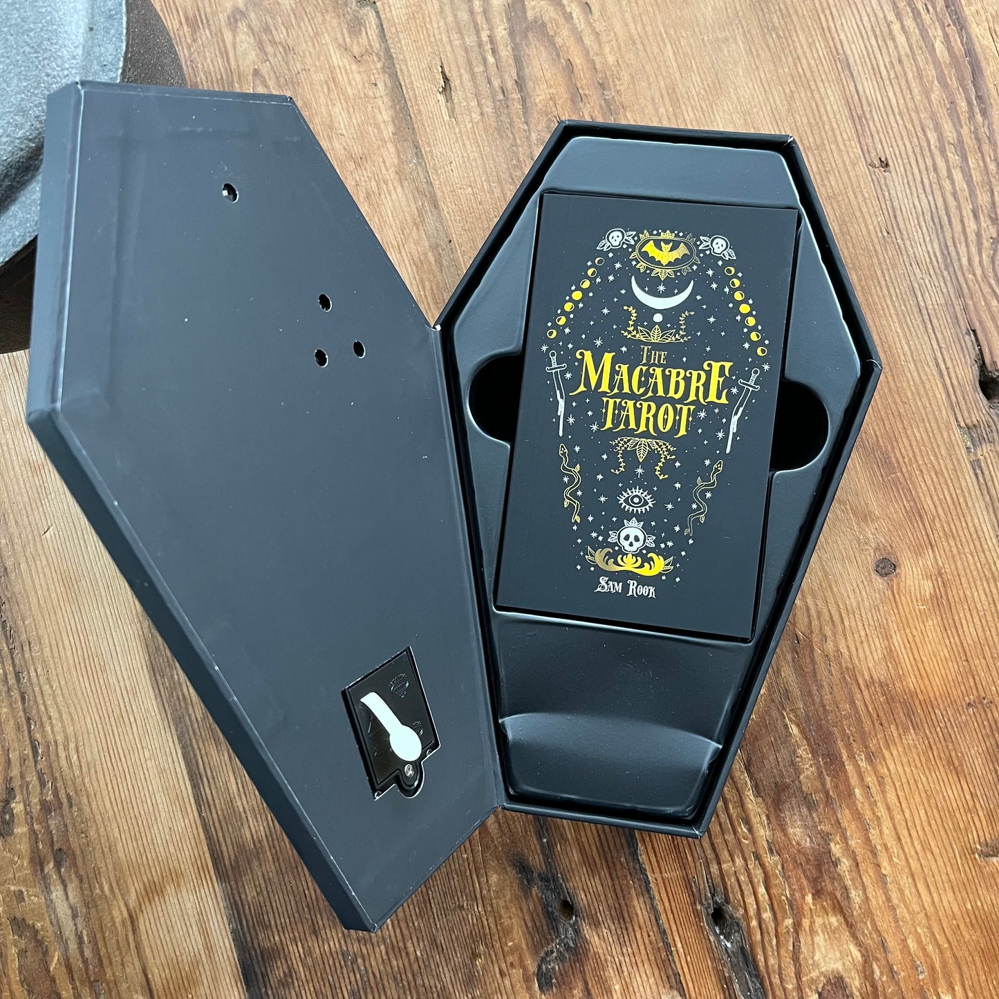 Black coffin-shaped box with 'The Macabre Tarot' design on a wooden surface
