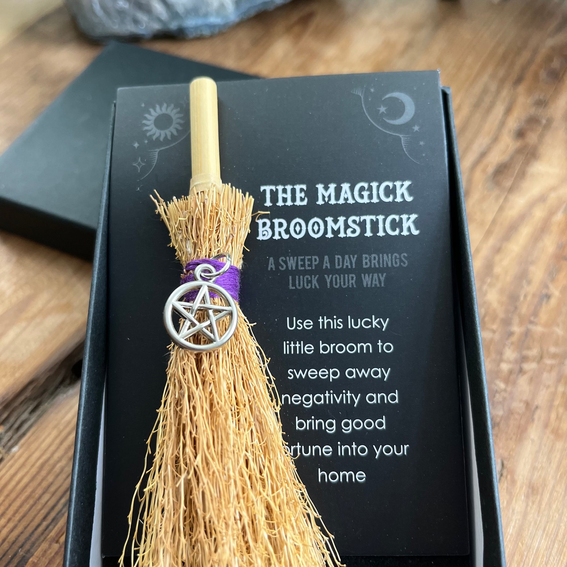 Magick broomstick with pentacle charm on a black card with text on a wooden surface