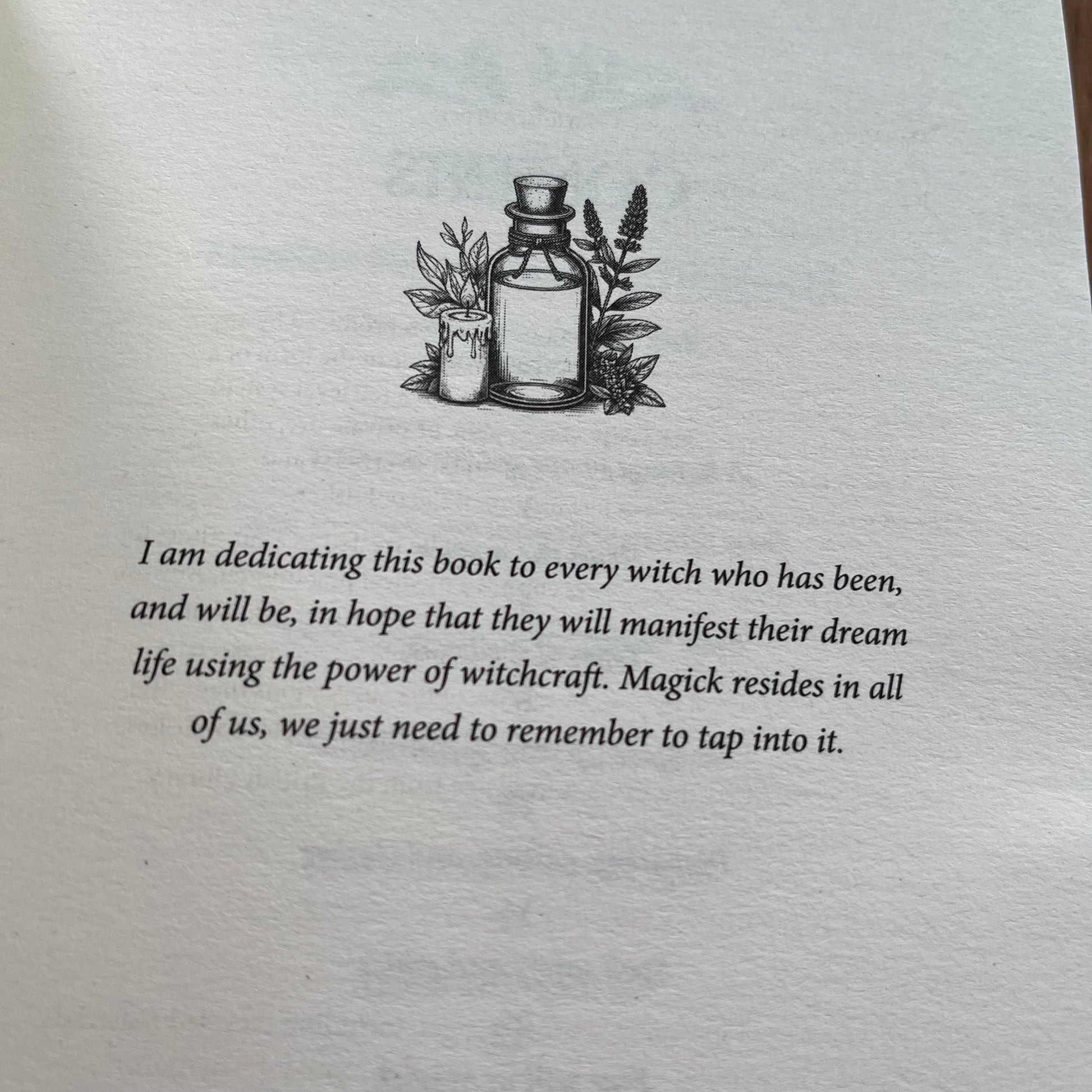 A close-up of a book's dedication page featuring a black ink illustration of a potion bottle and candle, with a handwritten-style dedication text below on aged off-white paper.