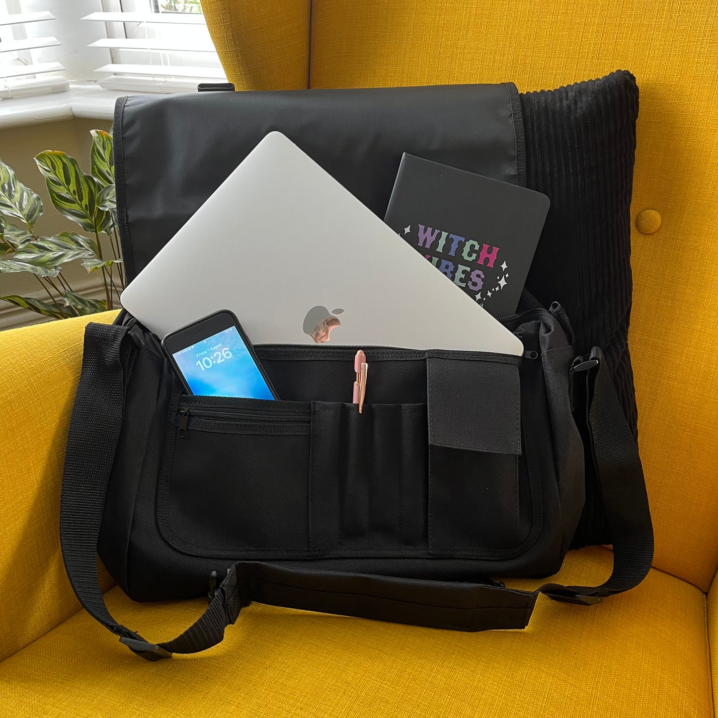 Black messenger bag with laptop, tablet, and books on a yellow couch