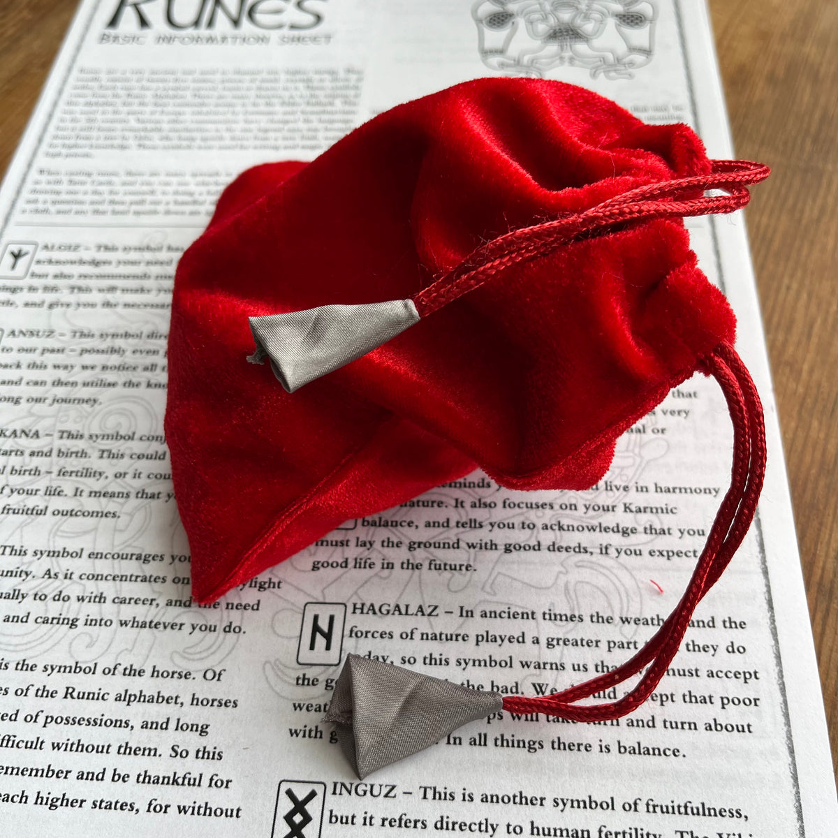 A small red velvet drawstring pouch with silver-toned metal accents, placed on top of an open book.