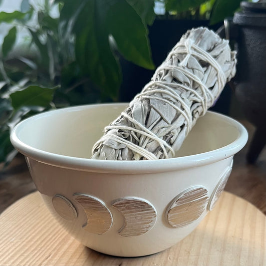 Decorative moon phase ceramic bowl on a wooden surface with plants in the background.