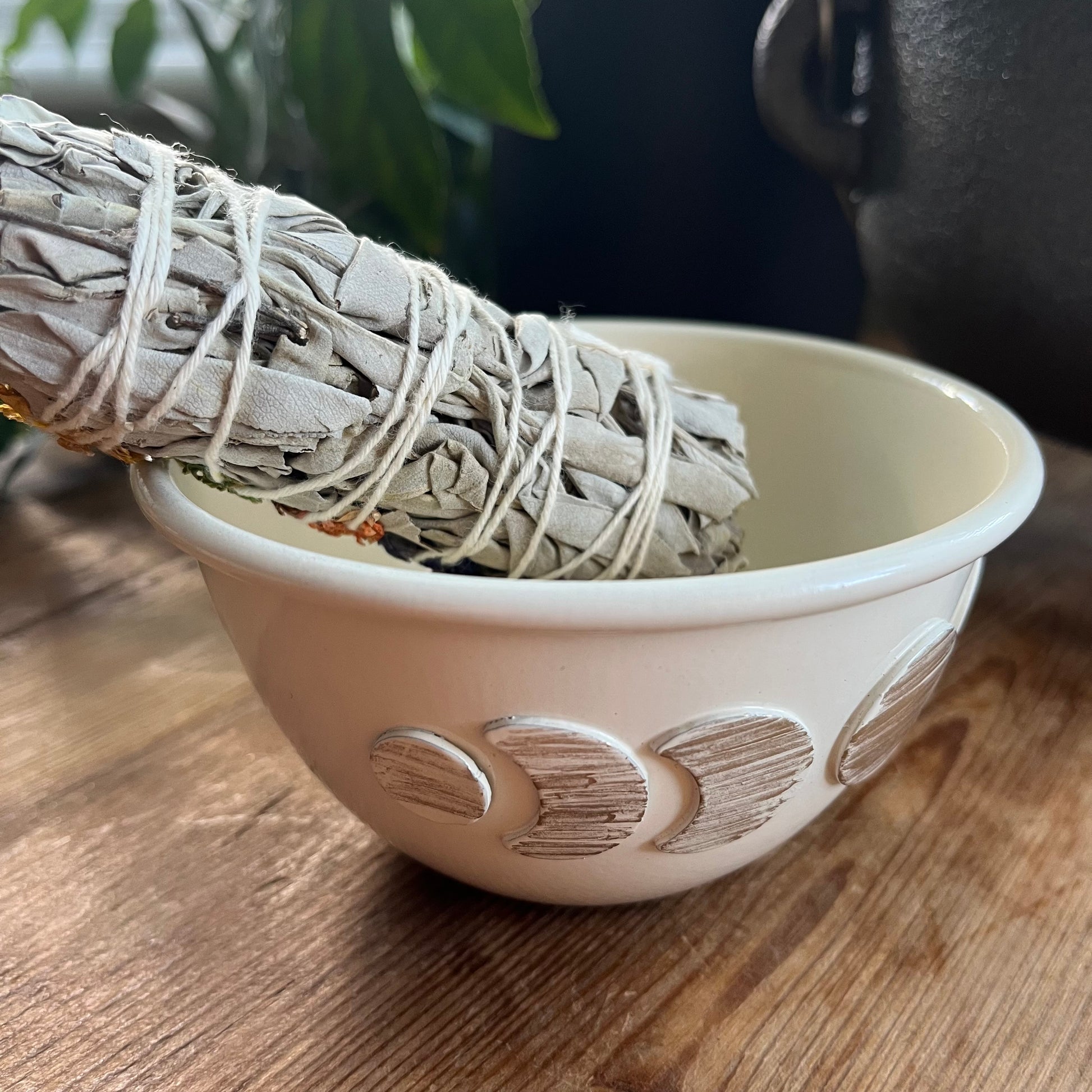 White decorative moon phase ceramic smudge bowl on a wooden surface